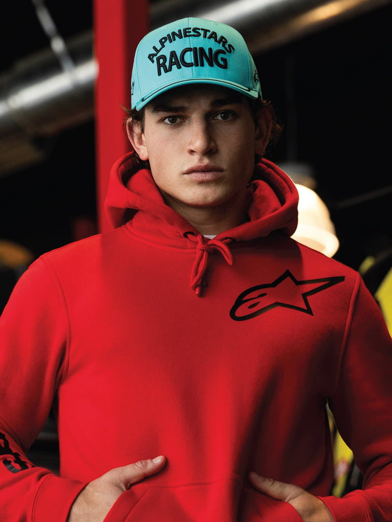 Alpinestars Luminary Hat, aqua-blå snapback med böjd skärm, svart 3D-broderi med texten 'ALPINESTARS RACING', bärs med en klarröd Alpinestars-hoodie, casual motorsport-livsstil streetwear