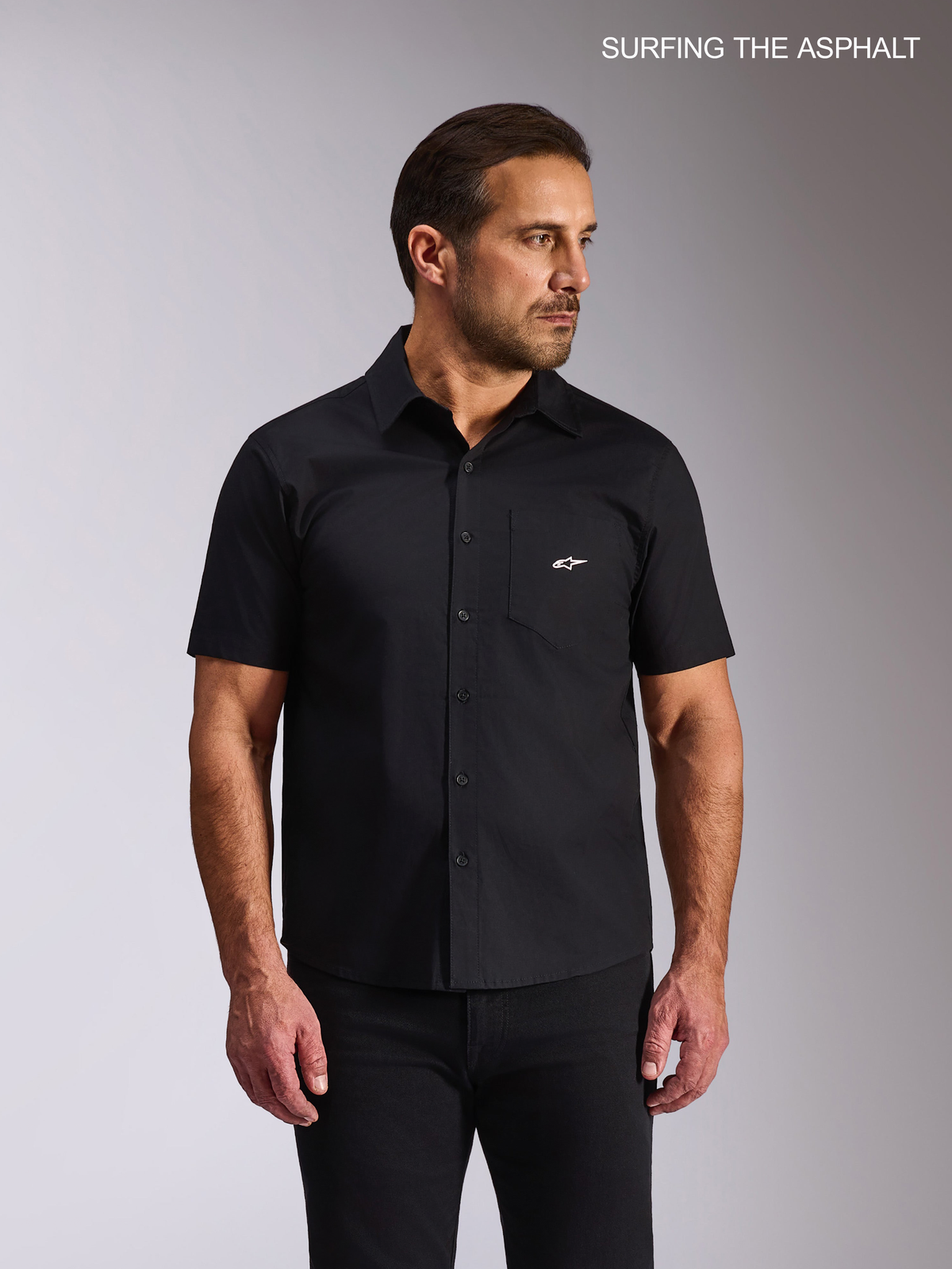 Alpinestars Strive Woven Skjorta, kortärmad vardagsskjorta i svart stretchpoplin med bröstficka och vit logga, bärs av en manlig modell