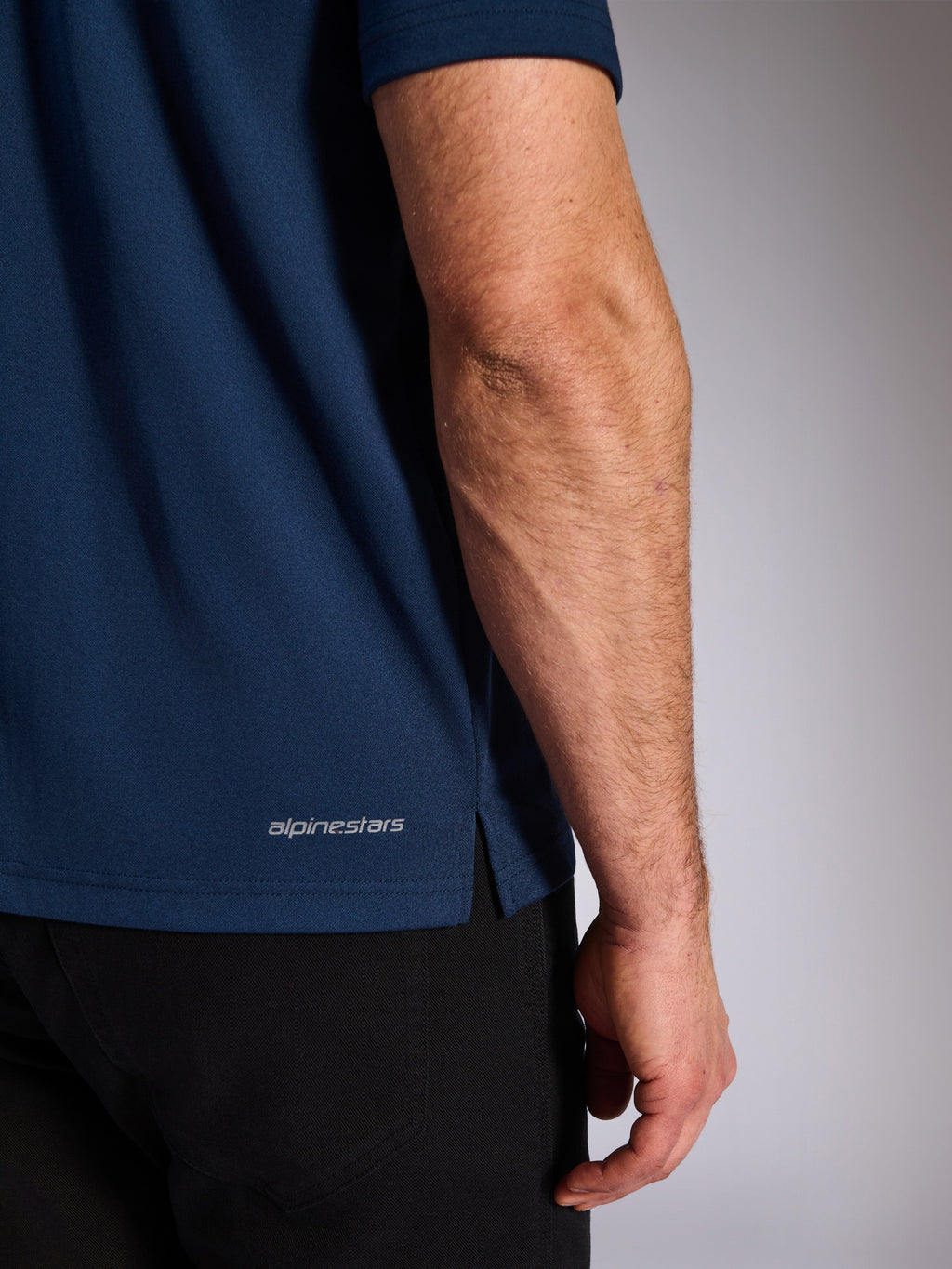 Alpinestars Impetus Sport Polo, marinblå, närbild på den nedre fållen som visar Alpinestars ordmärke och sidoslits, mock-mesh-stickad textur, vardagliga motorsport-sportkläder