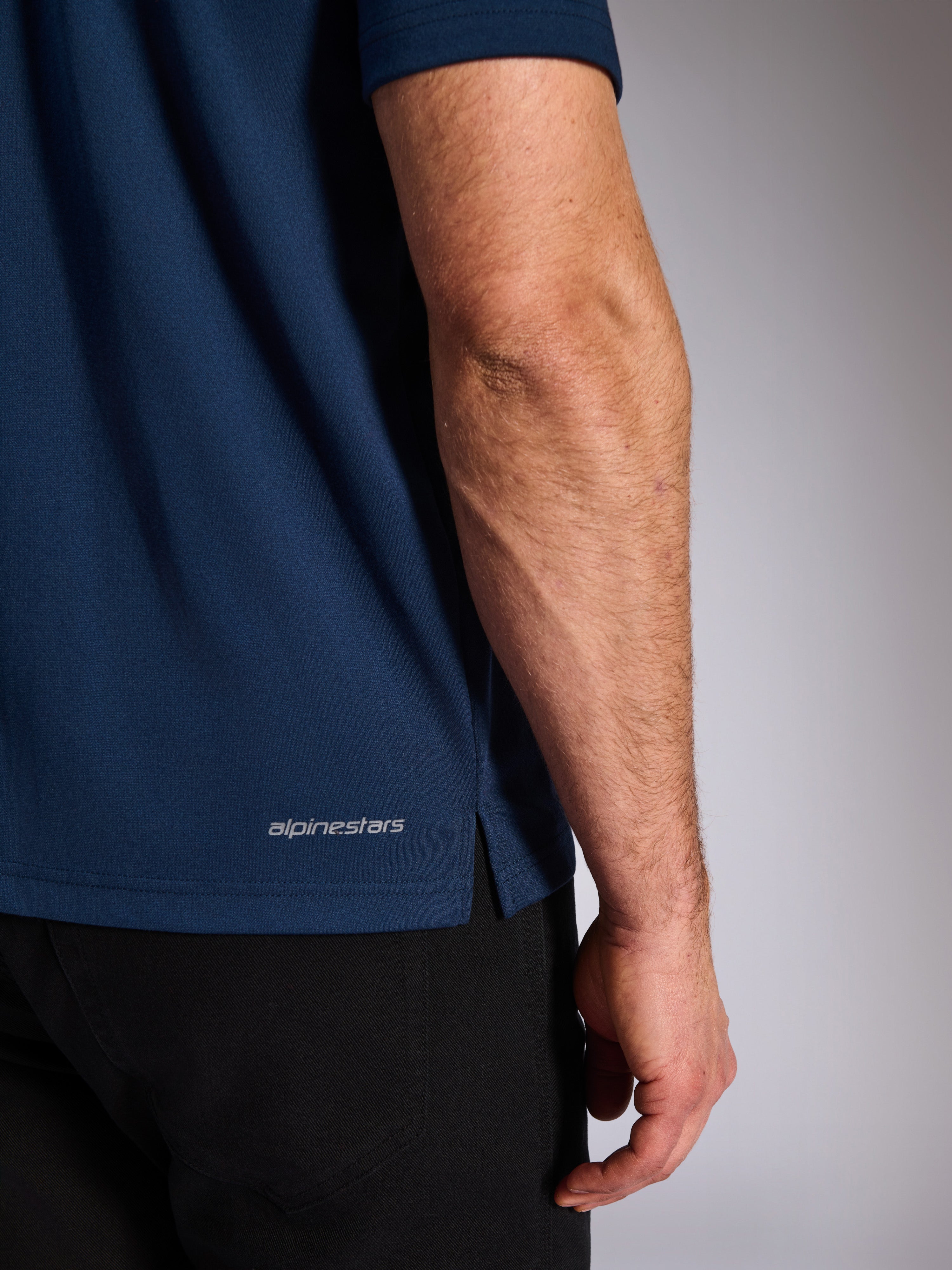 Alpinestars Impetus Sport Polo, marinblå, närbild på den nedre fållen som visar Alpinestars ordmärke och sidoslits, mock-mesh-stickad textur, vardagliga motorsport-sportkläder