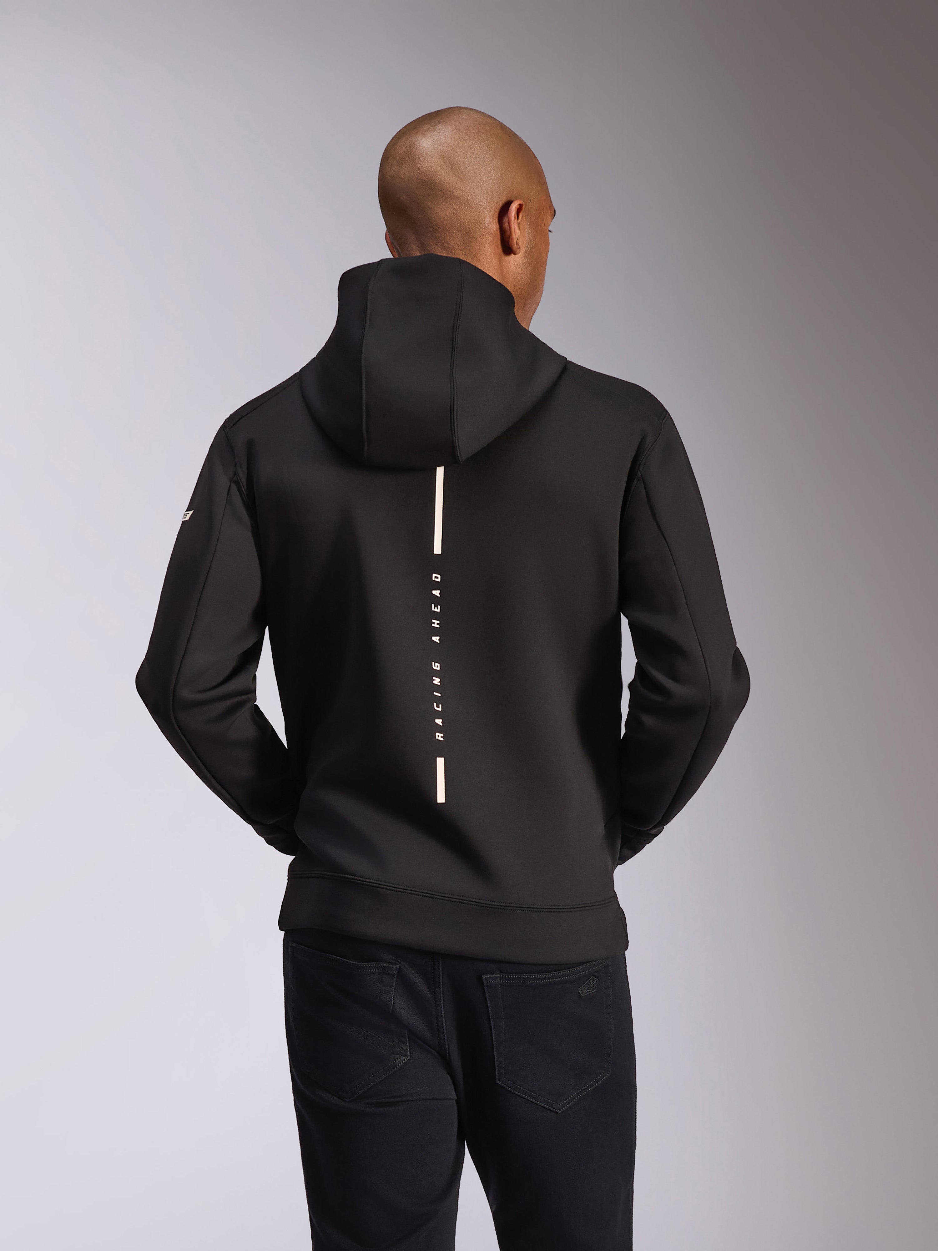 Alpinestars Insight huvtröja, sedd bakifrån, svart, vertikal vit rand med texten "RACING AHEAD", logotyp på ärmen, avslappnat motorsport-inspirerat streetwear