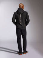 Alpinestars Insight Hoodie, svart, sedd bakifrån på modell, med en vertikal vit randlogotyp på ryggen och texten ”Racing Ahead”, vardaglig huvtröja i tri-blend dubbelsidig fleece, matchad med svarta byxor.