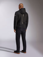 Alpinestars Insight Huvtröja, svart sportswear-huvtröja, vy bakifrån som visar en vertikal vit rand med 'RACING AHEAD'-logotyp, ärmlogotyp, kombinerad med svarta byxor och sneakers, avslappnad motorsportinspirerad design