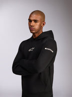 Alpinestars Insight Huvtröja, sportig huvtröja, svart, vit Astars-logotyp på bröstet och ordlogotyp på överarmen, modell som bär huvtröjan med armarna i kors, premiumkonstruktion i dubbelsidig fleece