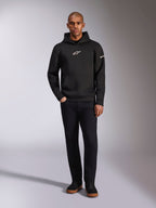 Alpinestars Insight Hoodie, svart huvtröja med vit Astars-logotyp på bröstet och ärmen, bärs av en modell med svarta byxor och svarta sneakers, avslappnad motorsportinspirerad streetwear