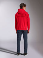 Alpinestars Emergent Oversized Hoodie, röd, sedd bakifrån på manlig modell, med ton-i-ton 3D-broderad Alpinestars-ordlogotyp, bärs med mörkblå jeans, casual motorsport-inspirerad streetwear