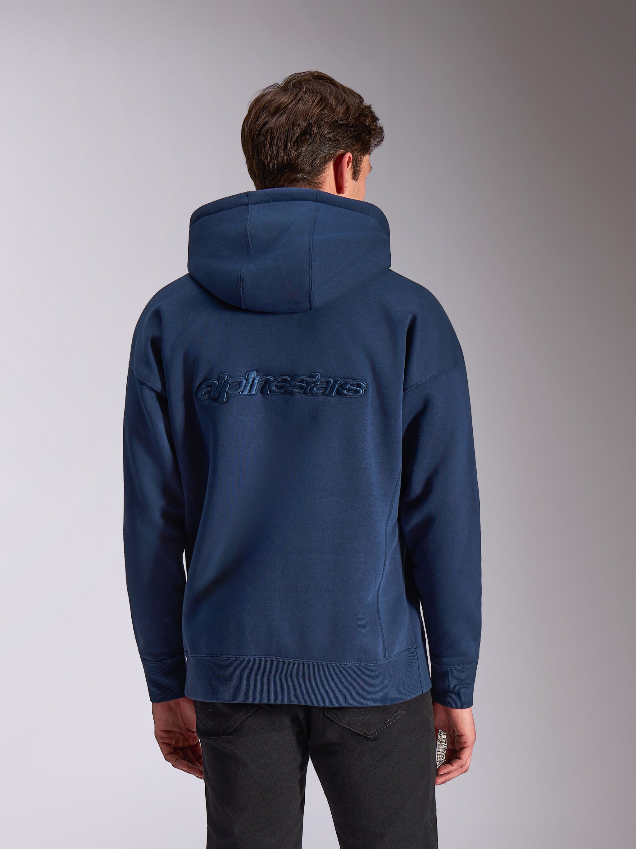 Alpinestars Emergent Oversized Hoodie, marinblå, baksida med ton-i-ton broderad Alpinestars-ordlogotyp, oversized passform, ledig huvtröja i fleece, huva med dragsnöre och ribbade muddar, motorsport-inspirerat streetwear.
