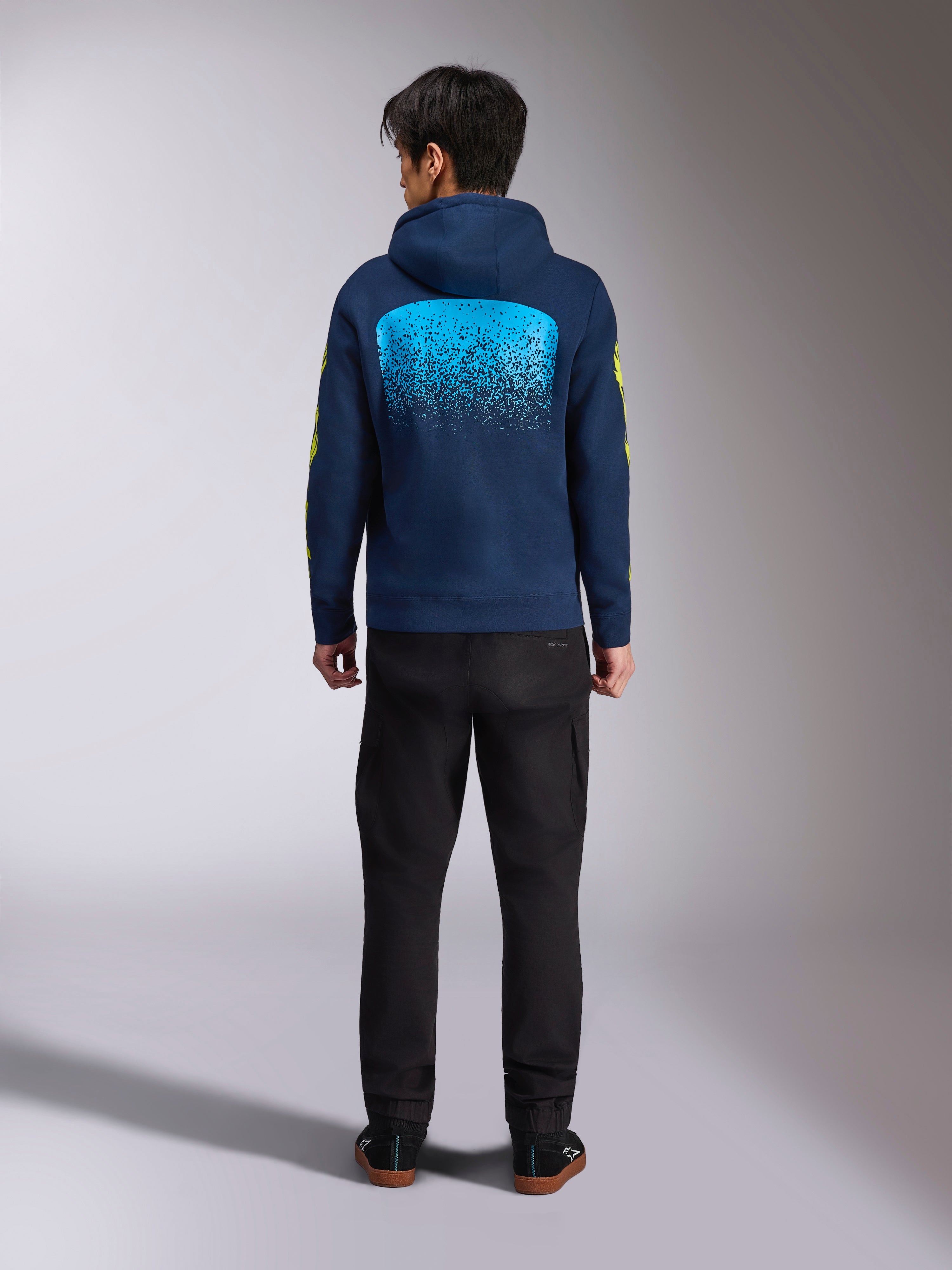 Alpinestars Obsessed Hoodie i marinblått, vy bakifrån med en stor cyanfärgad MX-graderingsgrafik och gula logotyper på ärmarna, avslappnad motorsportinspirerad pullover i fleece.