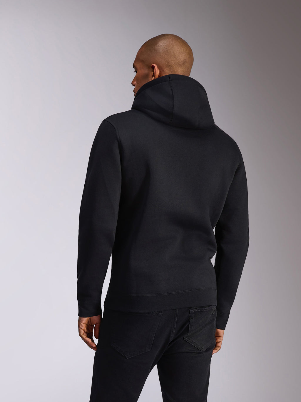 Alpinestars Ellipsoid Hoodie, svart, baksida av en person som bär en huvtröja i fleece, långa ärmar med ribbade muddar och fåll, stylad med svarta jeans, vardagliga motorsportinspirerade sportkläder