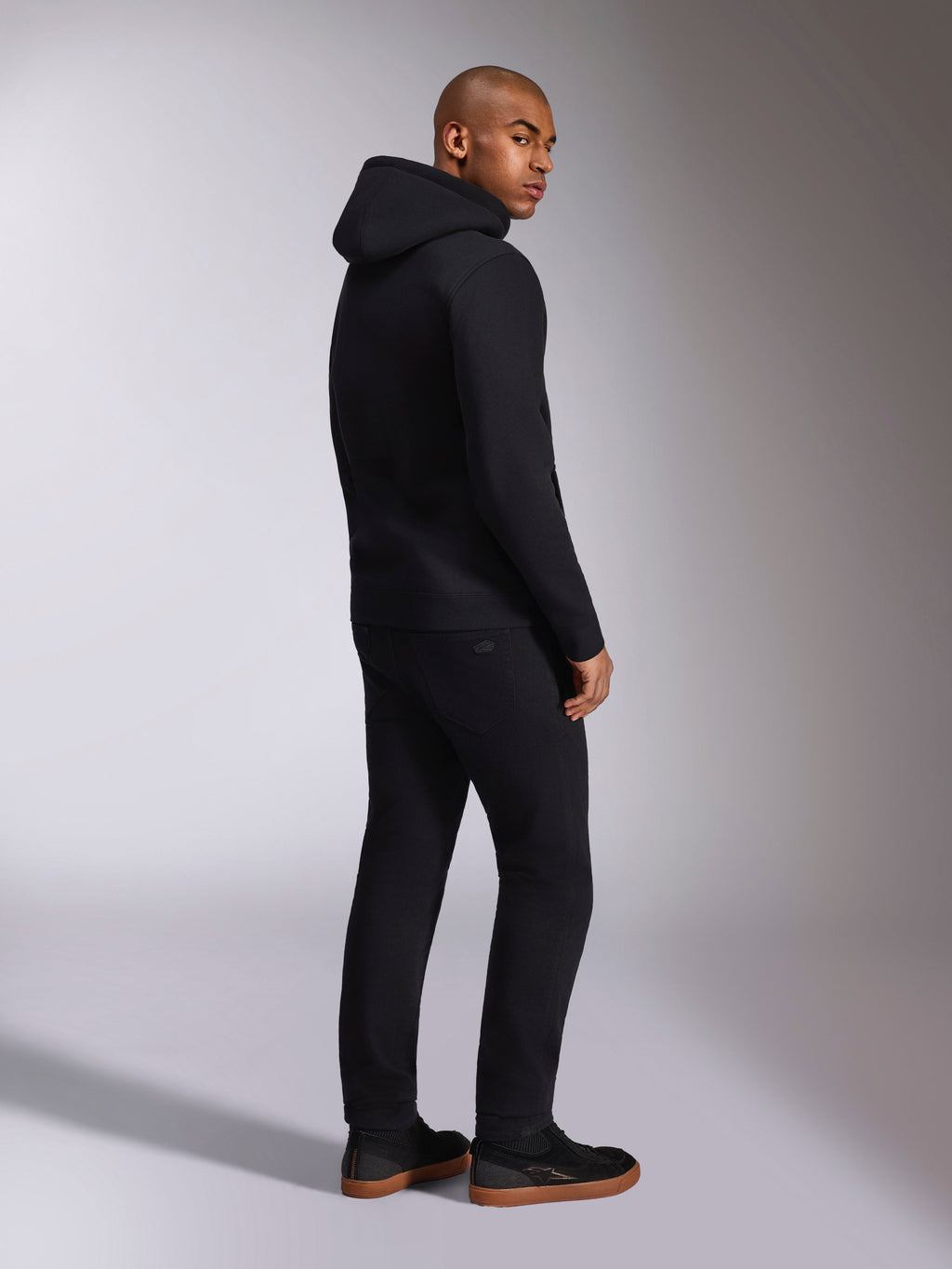 Alpinestars Ellipsoid Hoodie, svart casual streetwear, vy bakifrån på manlig modell, huvtröja i fleece med ribbade muddar och fåll, bärs med svarta byxor och sneakers, modern motorsportinspirerad design