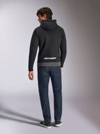 Alpinestars Parallel Hoodie, rear view of a man wearing a black and gunmetal color-blocked pullover fleece, white Alpinestars word logo on the lower back, paired with dark blue jeans, casual motorsport-inspired streetwear