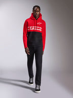 Alpinestars Parallel Huvtröja, färgblockad huvtröja i fleece, röd och svart, med vit Alpinestars-ordlogga över bröstet och Astars-logga på vänster bröst, bärs av en modell med svarta byxor och high-top sneakers, avslappnad motorsport-streetwear
