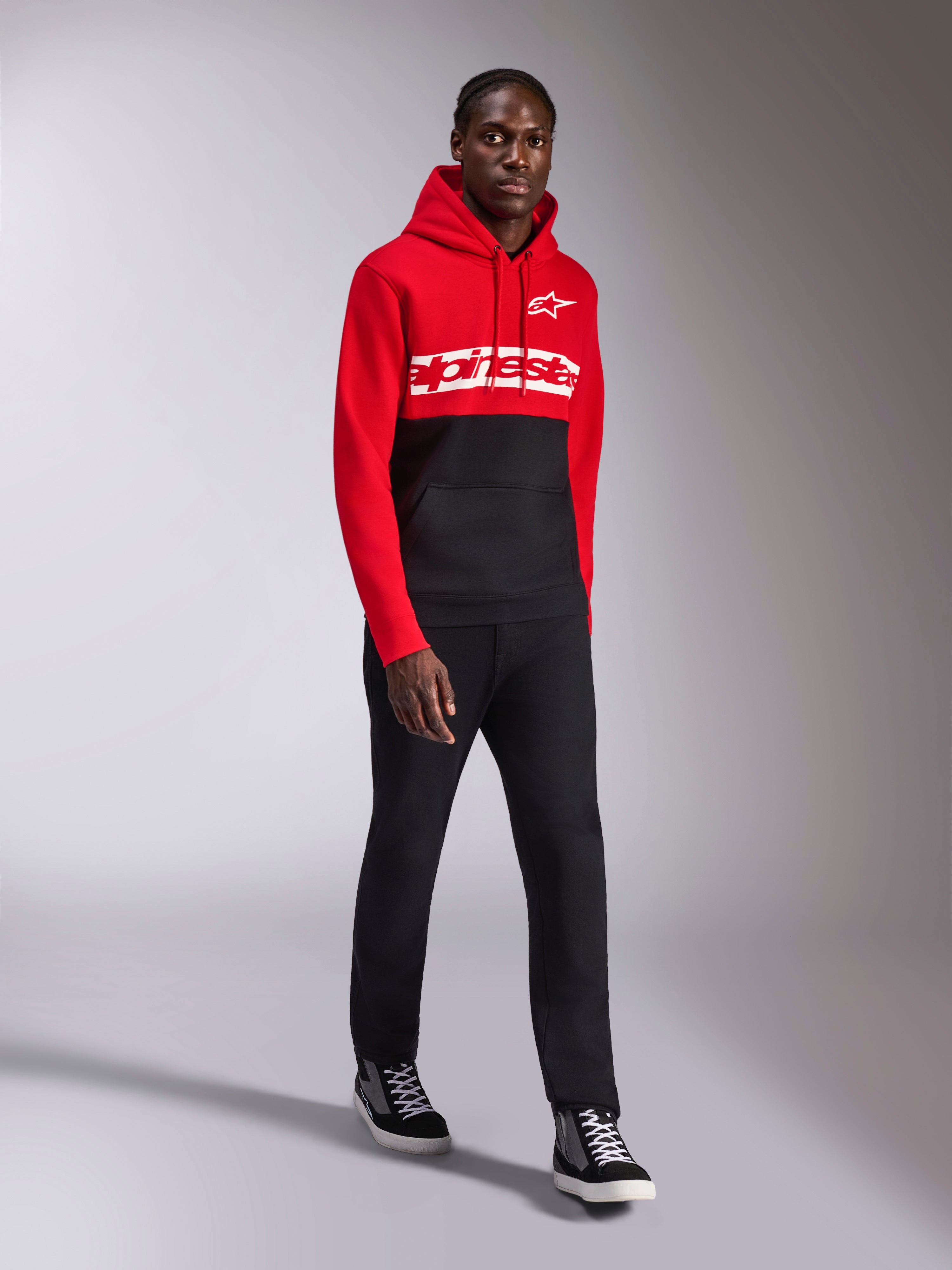 Alpinestars Parallel Hoodie, vardagliga sportkläder, röd och svart färgblockad design, med vit Alpinestars-ordlogga och stjärnlogotyp på bröstet, bärs med svarta byxor och sneakers, modern motorsportinspirerad look