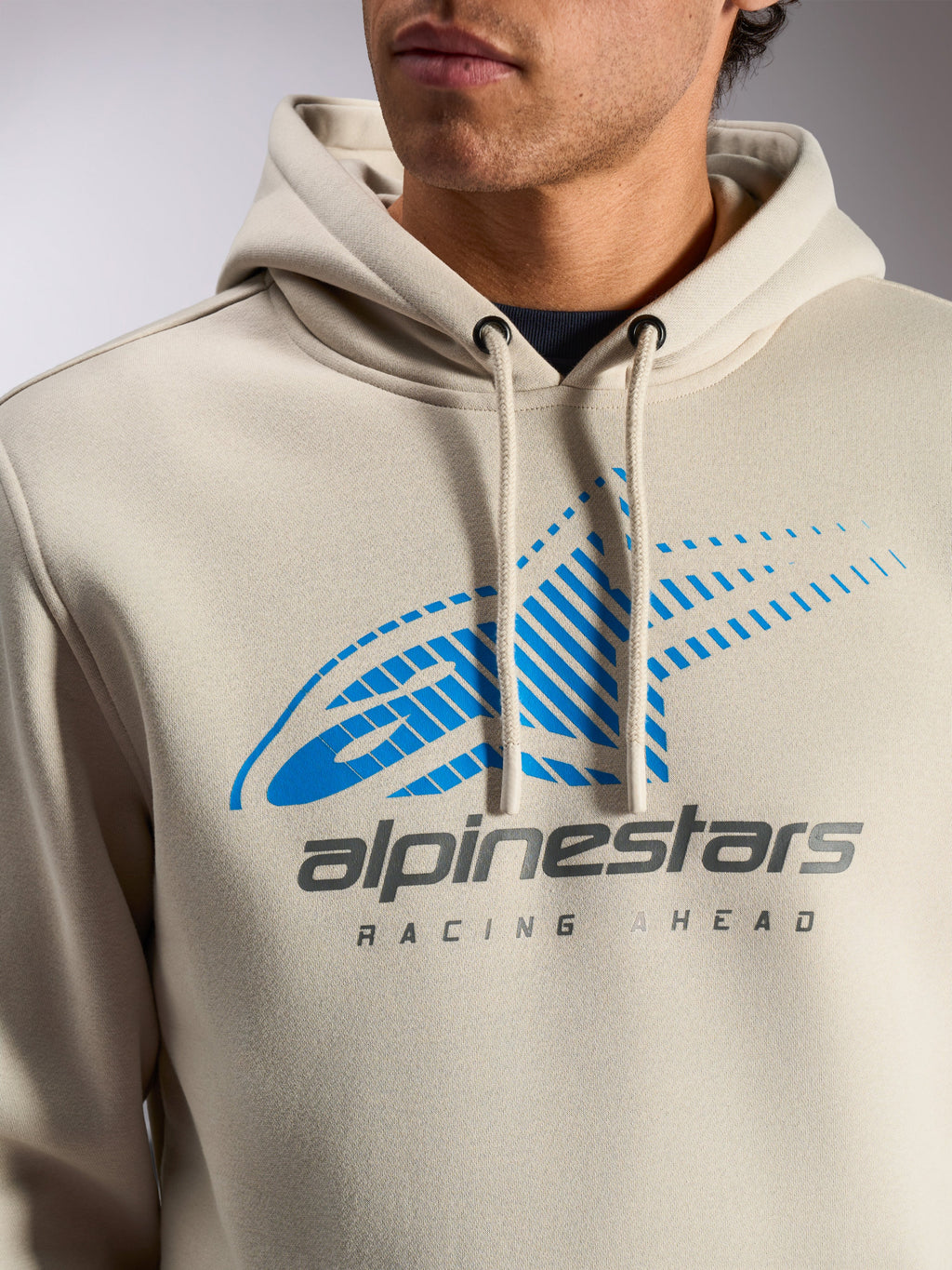 Alpinestars Pulse Hoodie, Off White casual streetwear-huvtröja, närbild på bröstet med blå och grå Astars Combo-logotyp med speed line-fade och texten 'Racing Ahead', huva med dragsko och doppade ändar.