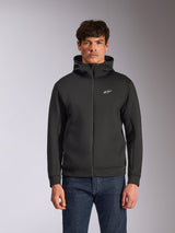 Alpinestars Cypher Hoodie, svart fleecehuvtröja med dragkedja fram, med en huva med hög krage, vit branding och en liten vit Astars-logotyp på bröstet, bärs av en modell i blå jeans, avslappnad motorsport-inspirerad streetwear.