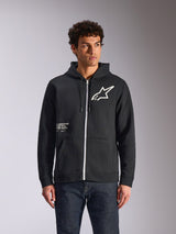 Alpinestars Transverse Hoodie, svart huvtröja i fleece med dragkedja fram, vit Astars-logotyp och One Goal-grafik på framsidan, bärs av en modell med mörka jeans, vardaglig motorsport-inspirerad streetwear