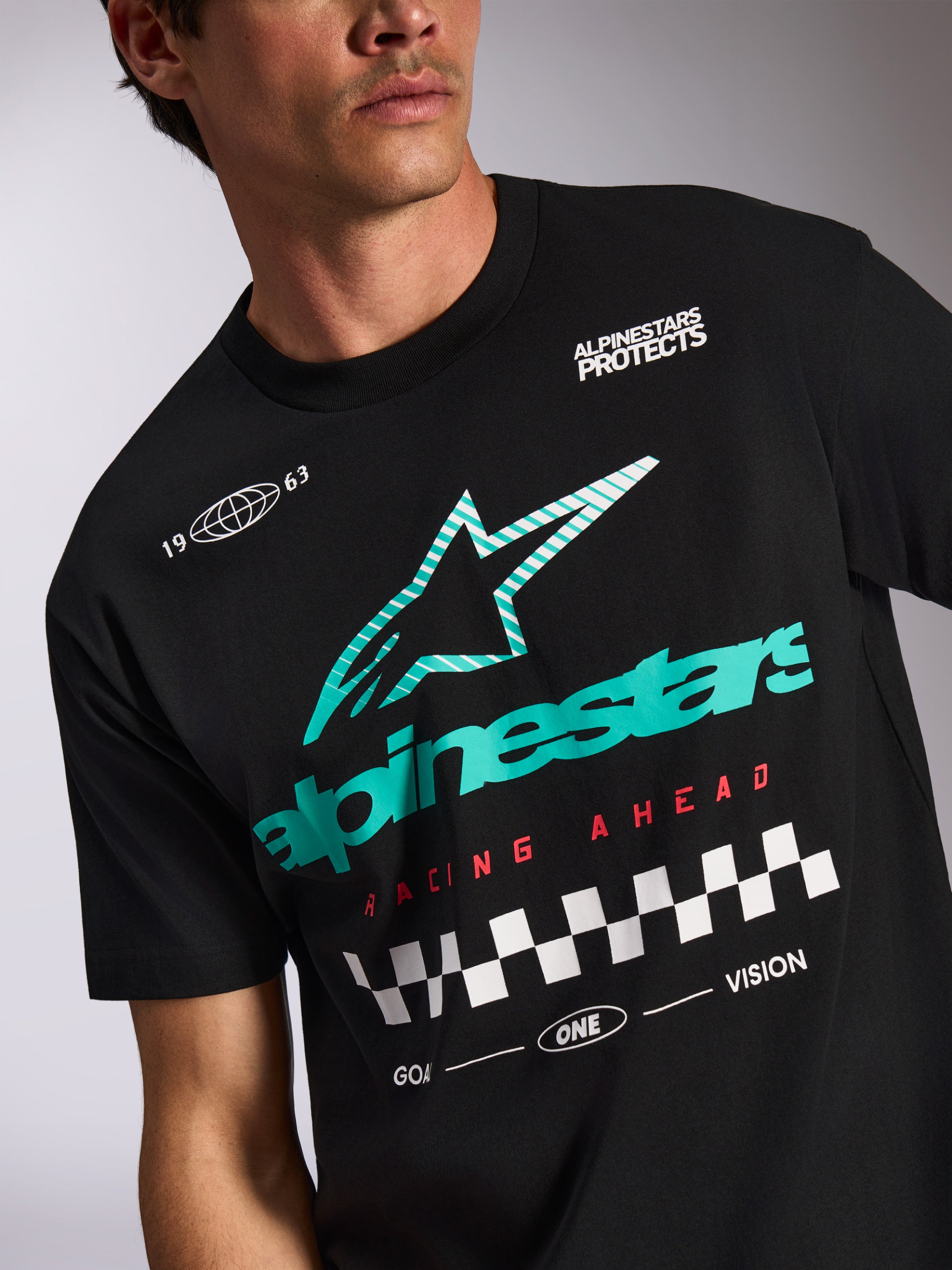 Alpinestars Aplomb Oversized CSF Tee, kortärmad t-shirt, svart, turkos- och vitrandig Astars-logotyp, röd 'Racing Ahead'-text med målflaggs-mönster, casual motorsport-streetwear