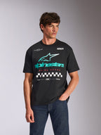 Alpinestars Aplomb Oversized CSF Tee, kortärmad t-shirt, svart, med en stor blågrön och vit Astars-kombinationslogga och rutig grafik, bärs av en manlig modell med mörkblå jeans, avslappnad motorsport-streetwear