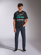 Alpinestars Aplomb Oversized CSF Tee, kortärmad t-shirt, svart, turkos tonad Astars-logotyp med röd "Racing Ahead"-text och rutmönstrade detaljer, bärs av modell med mörkblå jeans, avslappnat motorsport-streetwear