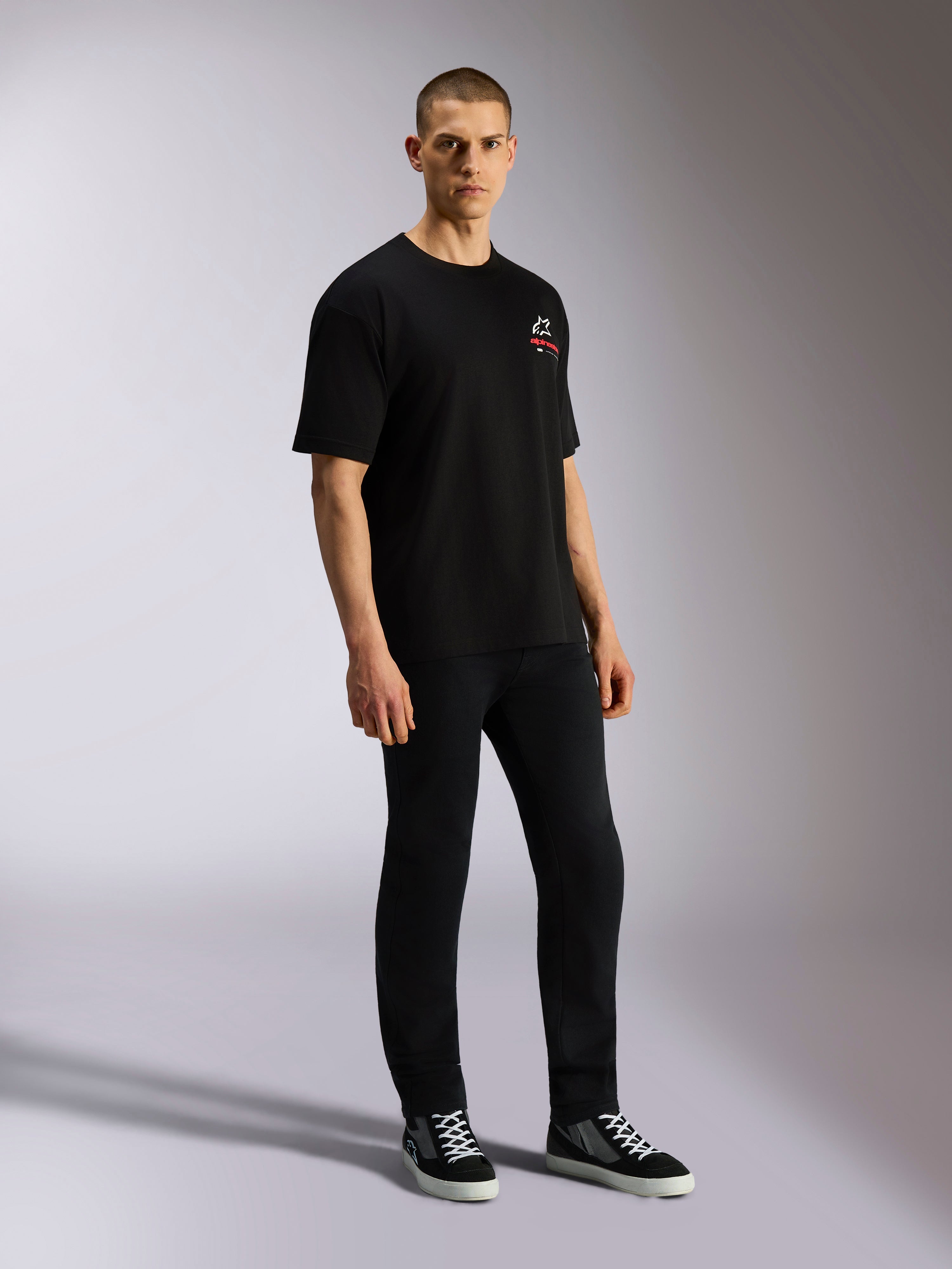 Alpinestars Overhang Oversized CSF Tee, kortärmad t-shirt, svart, med en vit och röd Astars-logotyp på framsidan, bärs av en modell med svarta byxor och sneakers, oversized avslappnad streetwear-design