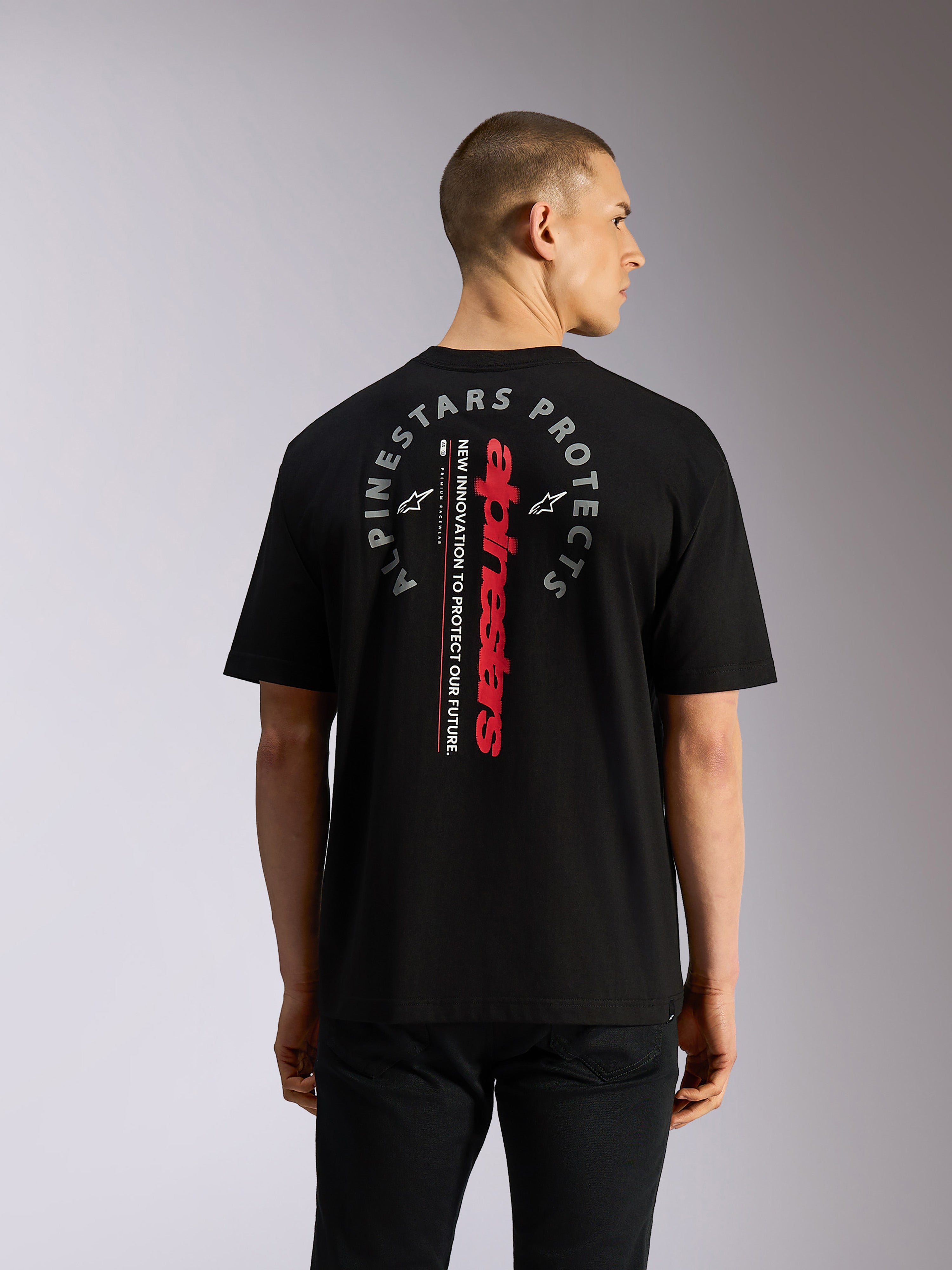 Alpinestars Overhang Oversized CSF Tee, kortärmad t-shirt, svart, baksida som visar vertikalt rött Alpinestars-ordmärke och cirkulär grå 'Alpinestars Protects'-grafik, casual motorsport-inspirerad streetwear