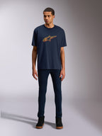 Alpinestars Alter Oversized CSF Tee, kortärmad t-shirt, marinblå, med Alpinestars stjärnlogotyp på framsidan i gul och orange färgförskjutning, bärs av en modell med mörka jeans och svarta sneakers, vardagliga sportkläder