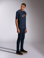 Alpinestars Alter Oversized CSF T-shirt, kortärmad t-shirt, marinblå, gul och orange Astars-logotyp, bärs av en modell med mörka jeans och svarta sneakers, avslappnad motorsportinspirerad streetwear