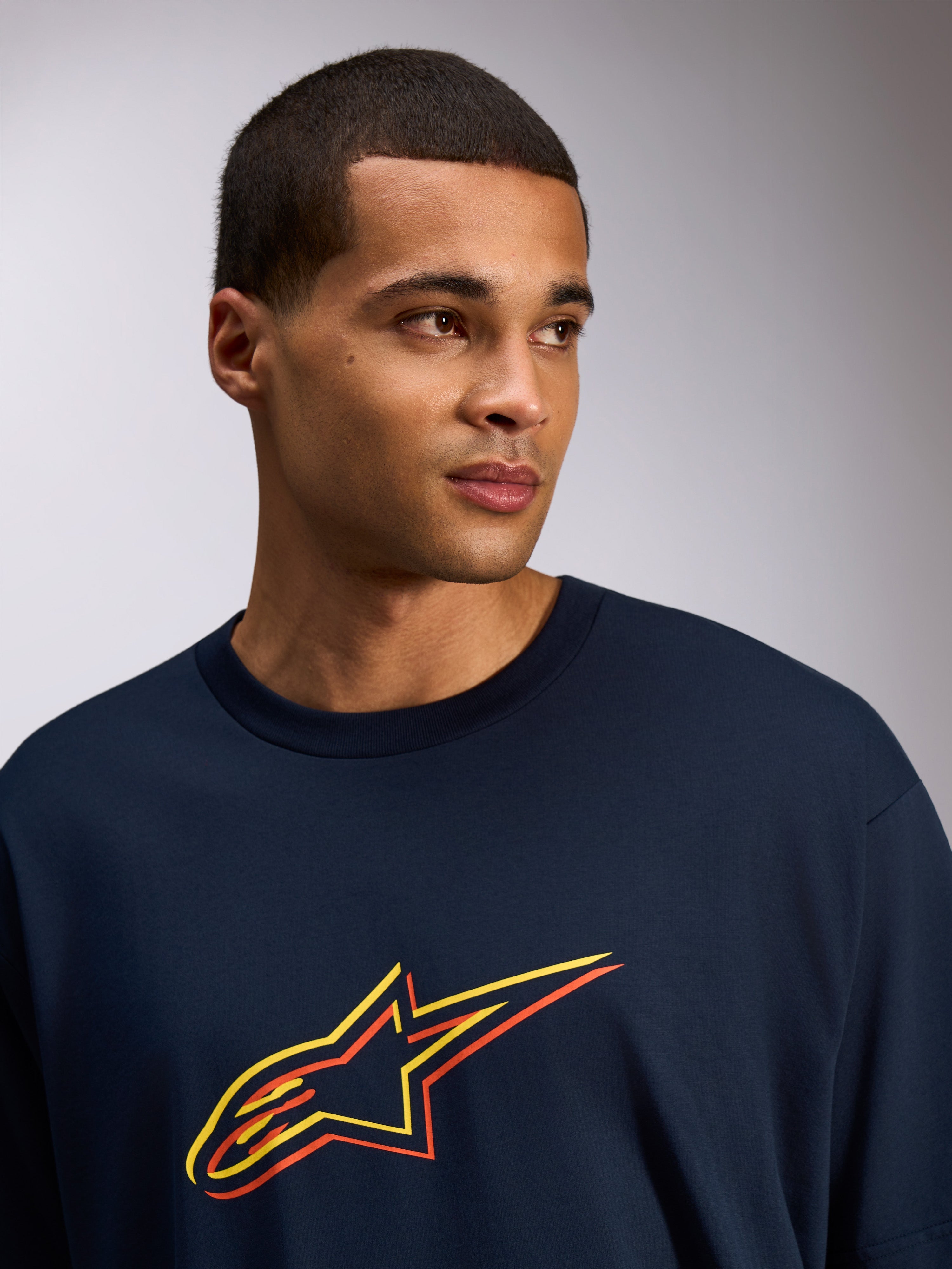 Alpinestars Alter Oversized CSF Tee, kortärmad t-shirt, marinblå, Astars-logotyp med gult och orange färgförskjutet tryck, casual streetwear-stil som bärs av en modell