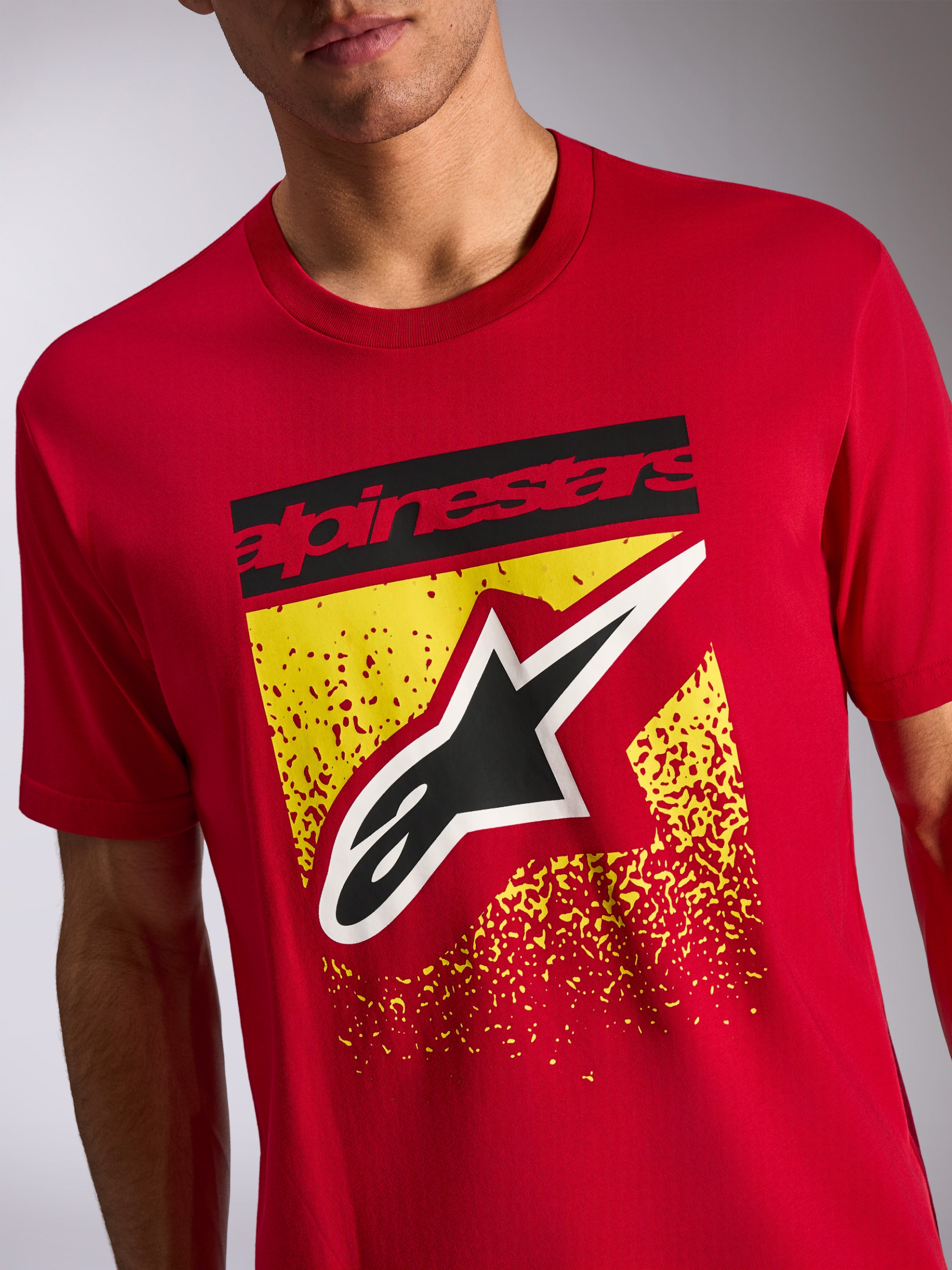 Alpinestars Noka CSF Tee, kortärmad t-shirt, röd, grafik på framsidan med svart Alpinestars-text och Astars-logotyp över gul spräcklig design, casual motorsport-streetwear