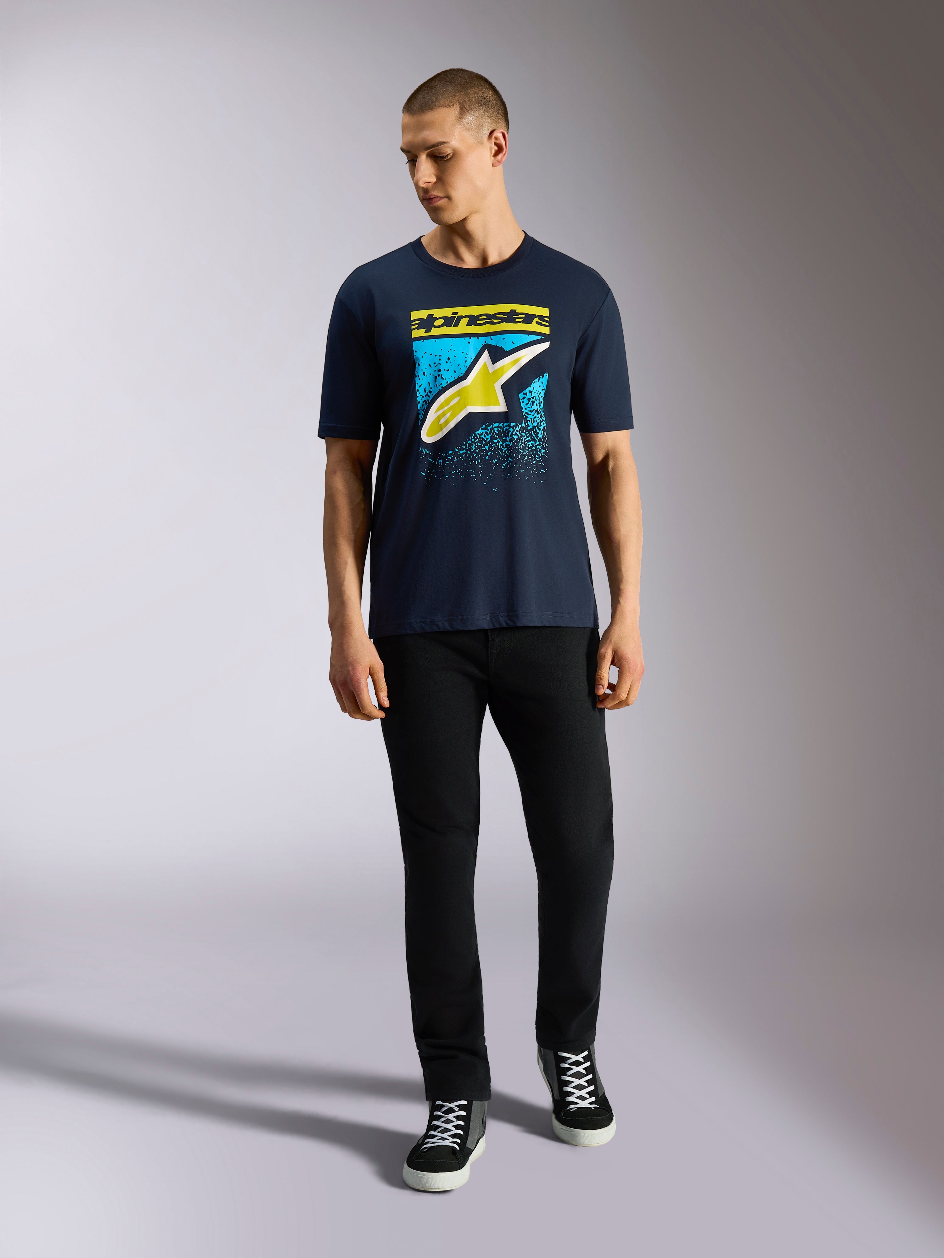 Alpinestars Noka CSF Tee, kortärmad t-shirt, marinblå, Astars-logotyp på framsidan med gul och ljusblå MX-gradering, bärs av en modell med svarta byxor, casual motorsport-streetwear
