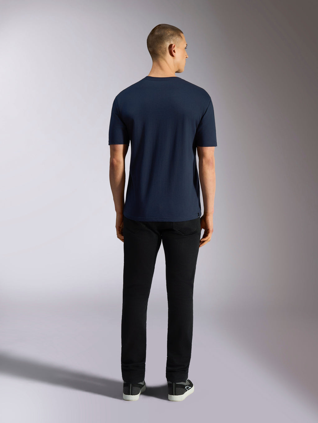 Alpinestars Noka CSF Tee, kortärmad t-shirt, marinblå, vy bakifrån av en man som bär t-shirten kombinerad med svarta byxor och sneakers, vardaglig motorsport-streetwear