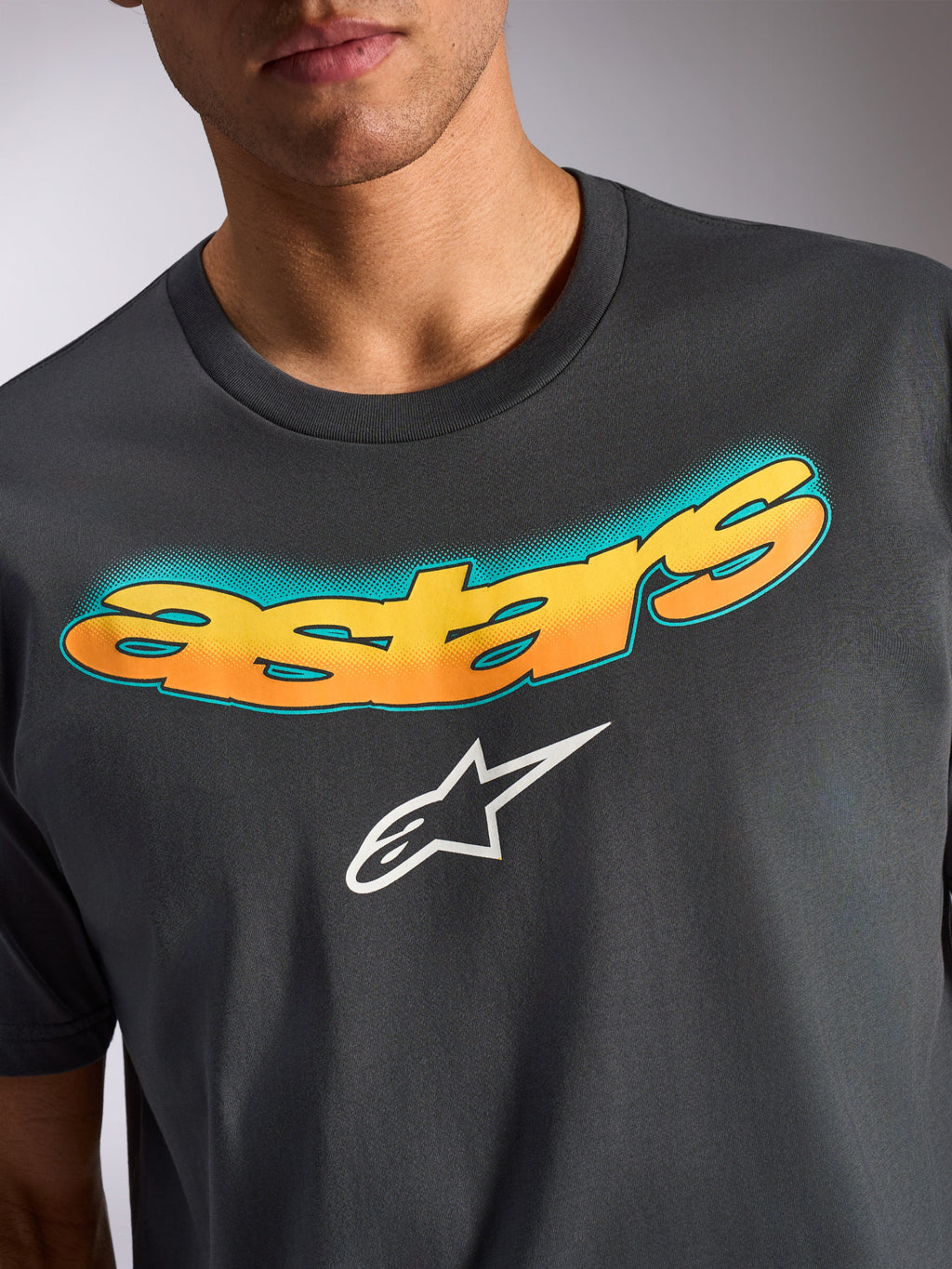Alpinestars Ellipsoid CSF Tee, kortärmad t-shirt, mörkgrå, böjd 'astars'-text med gul och orange färggradient och turkost prickmönster, vit Alpinestars stjärnlogotyp, avslappnade motorsportinspirerade kläder