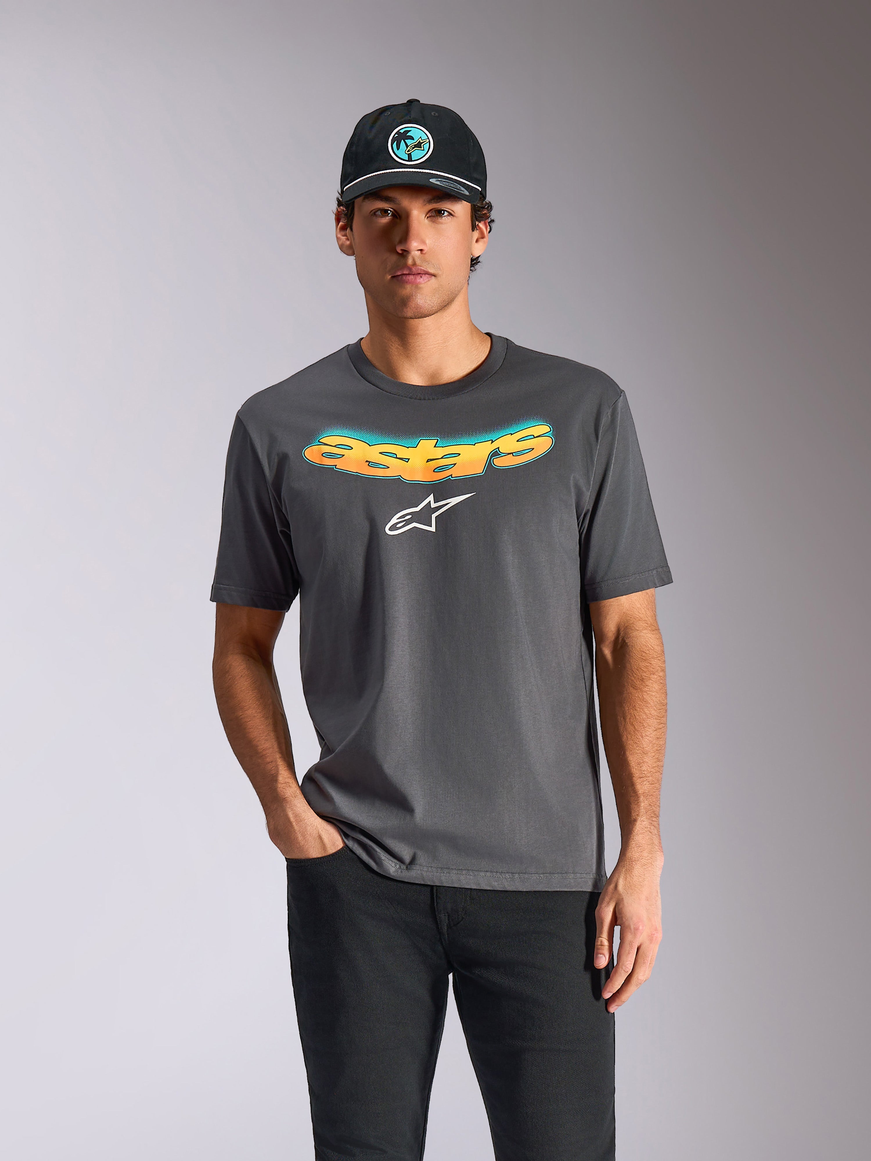 Alpinestars Ellipsoid CSF Tee, kortärmad t-shirt, charcoal-grå, böjd "astars"-text med orange och blå färggradient och vit logotyp, bärs av en modell med svart keps och byxor, casual motorsport-streetwear