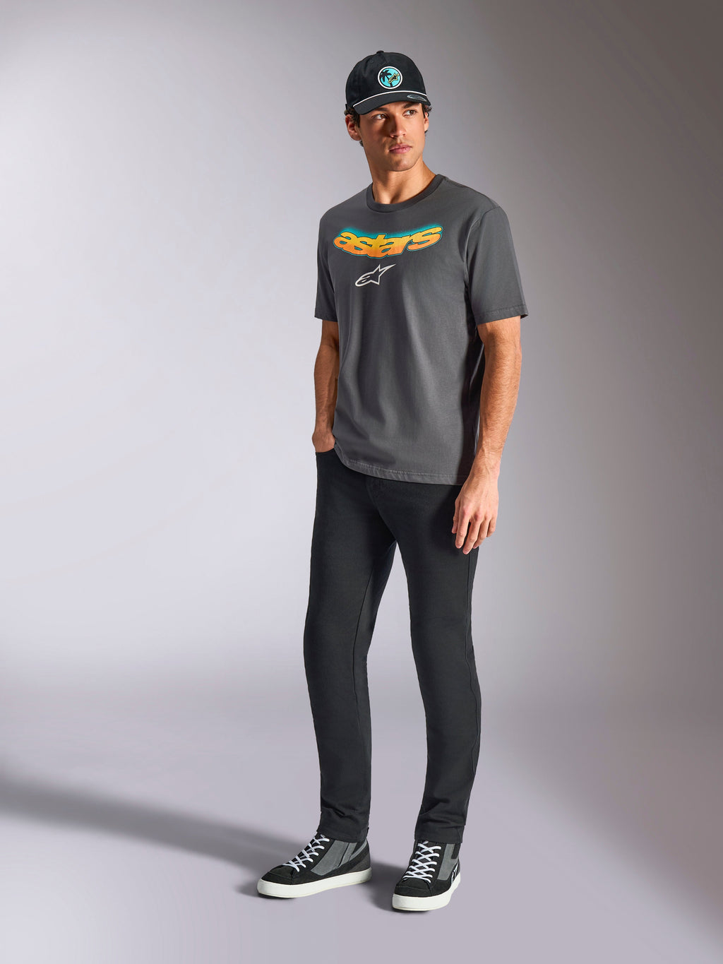 Alpinestars Ellipsoid CSF Tee, kortärmad t-shirt, kolgrå, med böjd Astars-text i färggradient och vit logotyp, bärs av modell med svarta byxor och keps, avslappnad motorsport-streetwear
