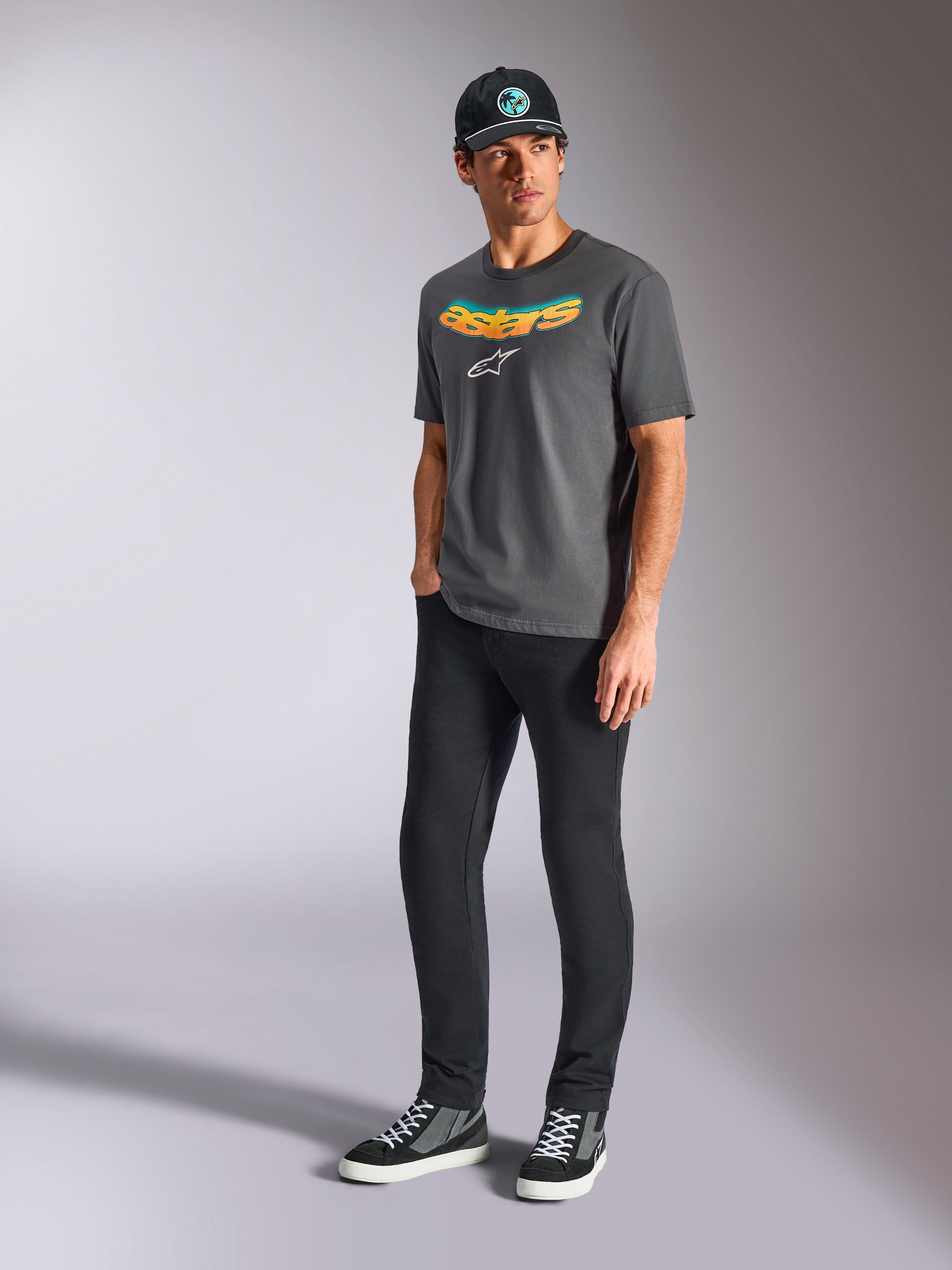 Alpinestars Ellipsoid CSF Tee, kortärmad t-shirt, kolgrå, med böjd Astars-text i färggradient och vit logotyp, bärs av modell med svarta byxor och keps, avslappnad motorsport-streetwear