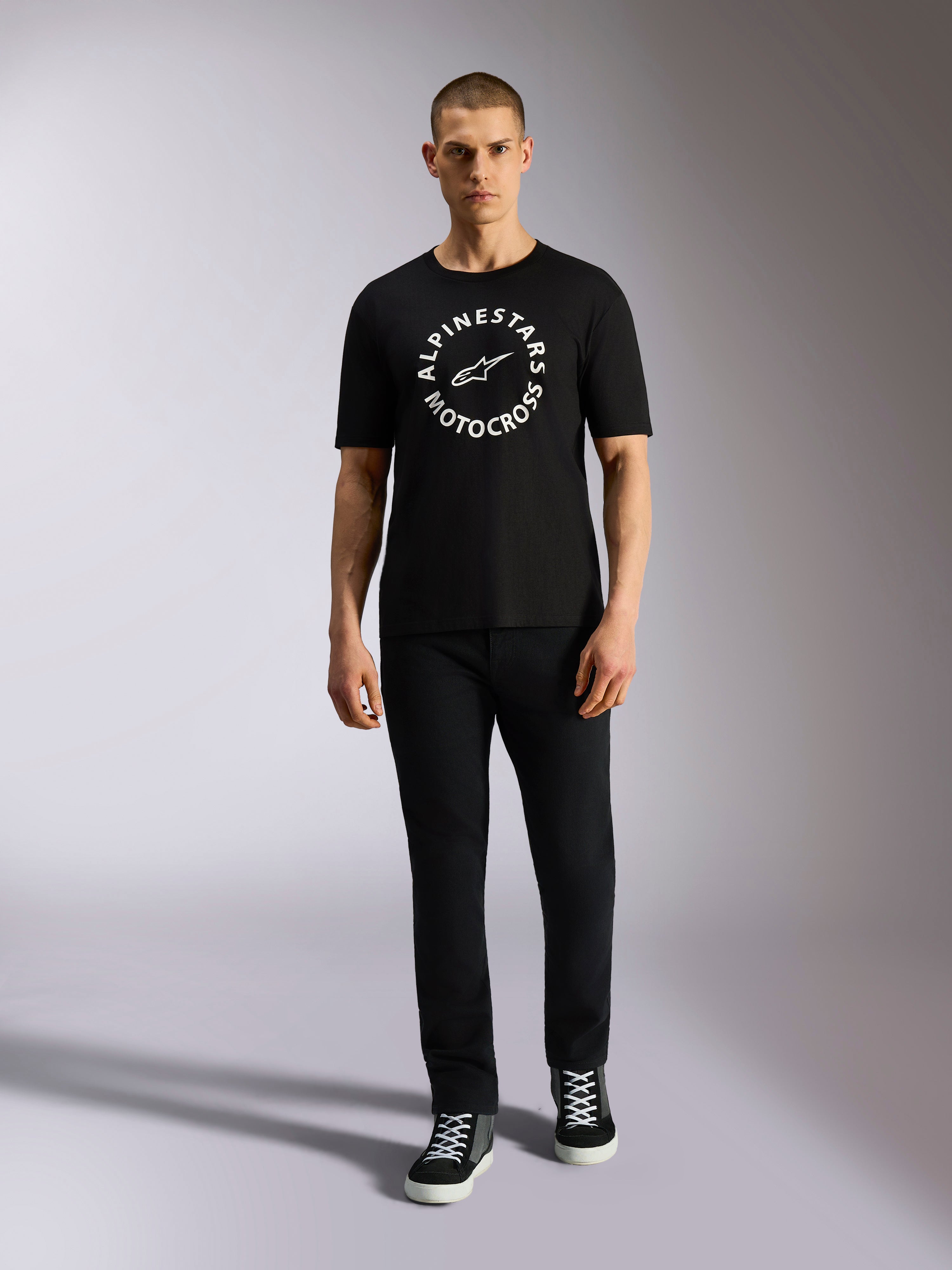 Alpinestars MX CSF Tee, kortärmad T-shirt, svart, vit cirkulär Alpinestars Motocross-grafik, bärs av modell med svarta byxor och sneakers, casual motorsport-streetwear