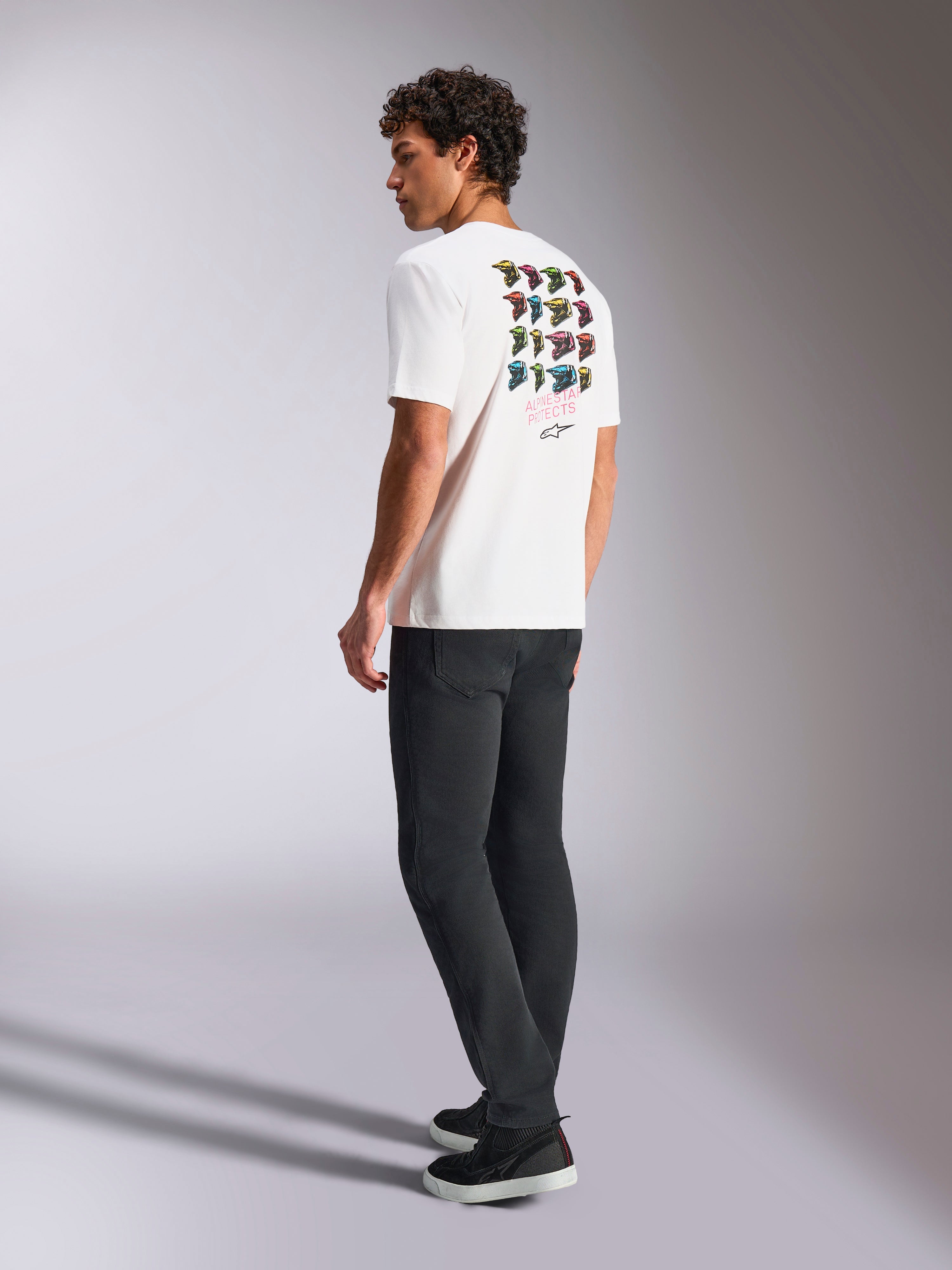 Alpinestars Pop Helmet CSF Tee, Short Sleeve T-Shirt, White, back view on model showing colorful M10 helmet graphic art, styled with dark pants and black sneakers, casual motorsport-inspired streetwear
