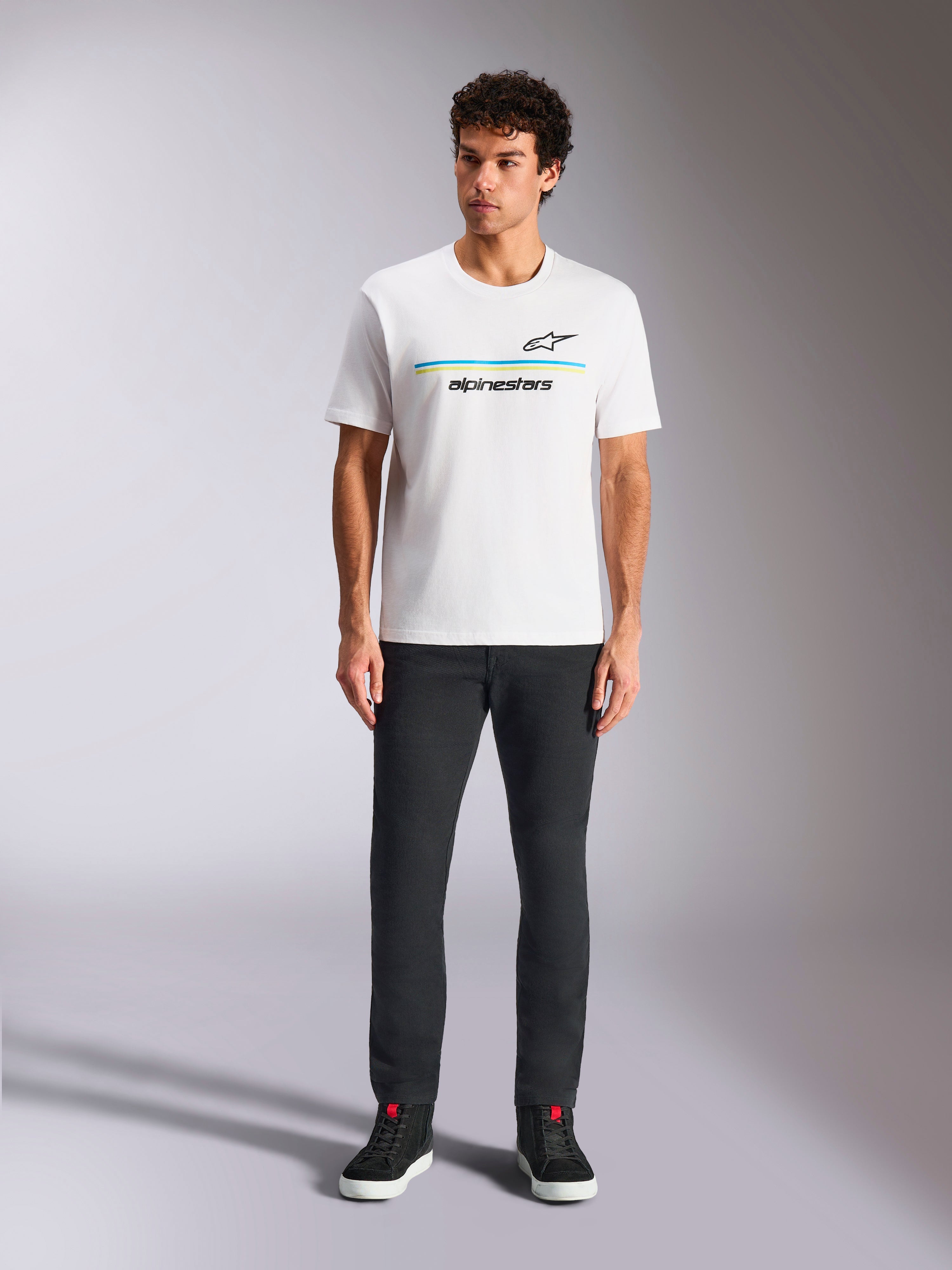 Alpinestars Lanes CSF Tee, kortärmad t-shirt, vit, blå och gul randig logotypgrafik, bärs av modell med svarta byxor och sneakers, casual motorsport-streetwear