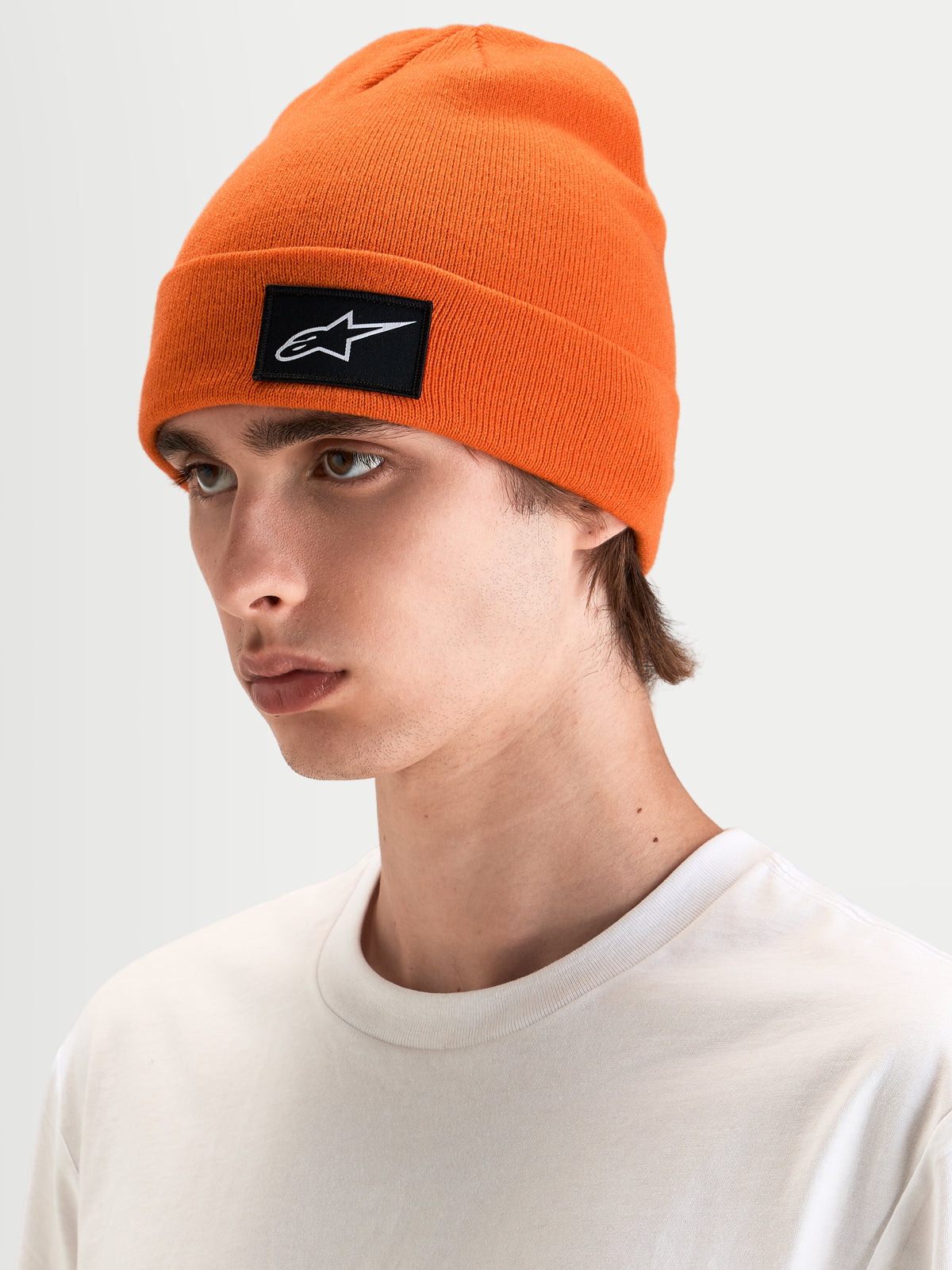 Alpinestars Augment Cuff mössa, orange stickad mössa med en svart och vit vävd Astars-logopatch, bars av en modell i vardagskläder