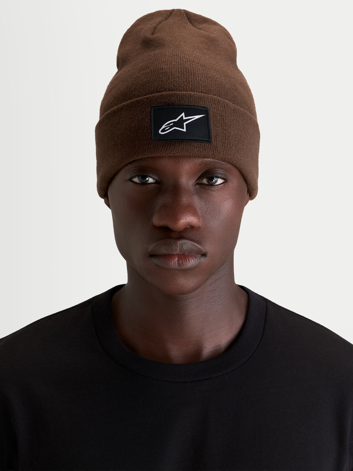 Alpinestars Augment Cuff mössa, brun sportswear-mössa med vävd logopatch, bärs av en modell i svart t-shirt