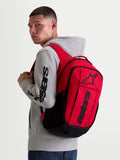 Alpinestars GFX Boss ryggsäck, röd och svart sportswear-ryggsäck för vardagsbruk, 20L kapacitet, slitstark 600D polyester, upphöjd silikontryckt Astars-logotyp, visas på en modell i en grå huvtröja.