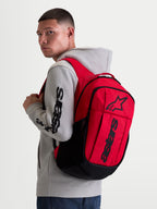 Alpinestars GFX Boss ryggsäck, röd och svart sportswear-ryggsäck för vardagsbruk, 20L kapacitet, slitstark 600D polyester, upphöjd silikontryckt Astars-logotyp, visas på en modell i en grå huvtröja.
