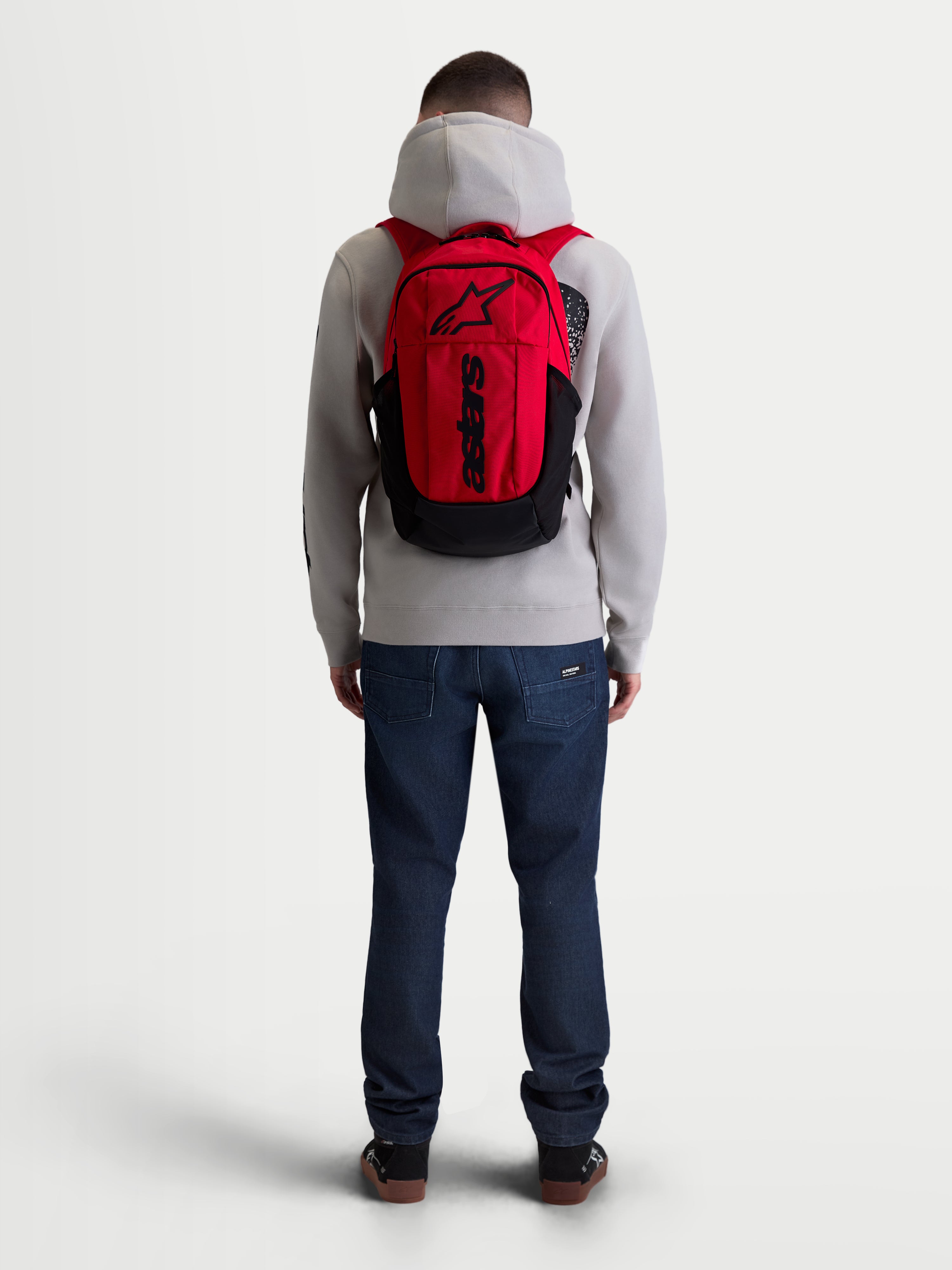 Alpinestars GFX Boss ryggsäck, 20L urban sportswear-ryggsäck, röd och svart, sedd bakifrån på modell. Slitstark 600D polyesterkonstruktion med invändigt laptopfack, vadderade axelremmar i luftmesh och upphöjd silikongrafik.