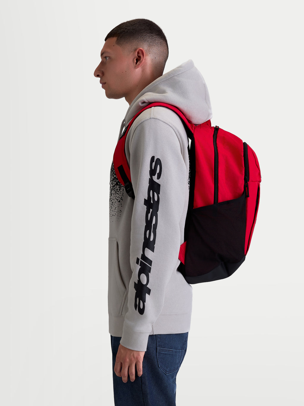 Alpinestars GFX Boss ryggsäck, röd och svart 20L sportryggsäck i hållbar 600D polyester med sidofickor i mesh för vattenflaskor och vadderade axelremmar, visas på modell för urban pendling och vardagsbruk.