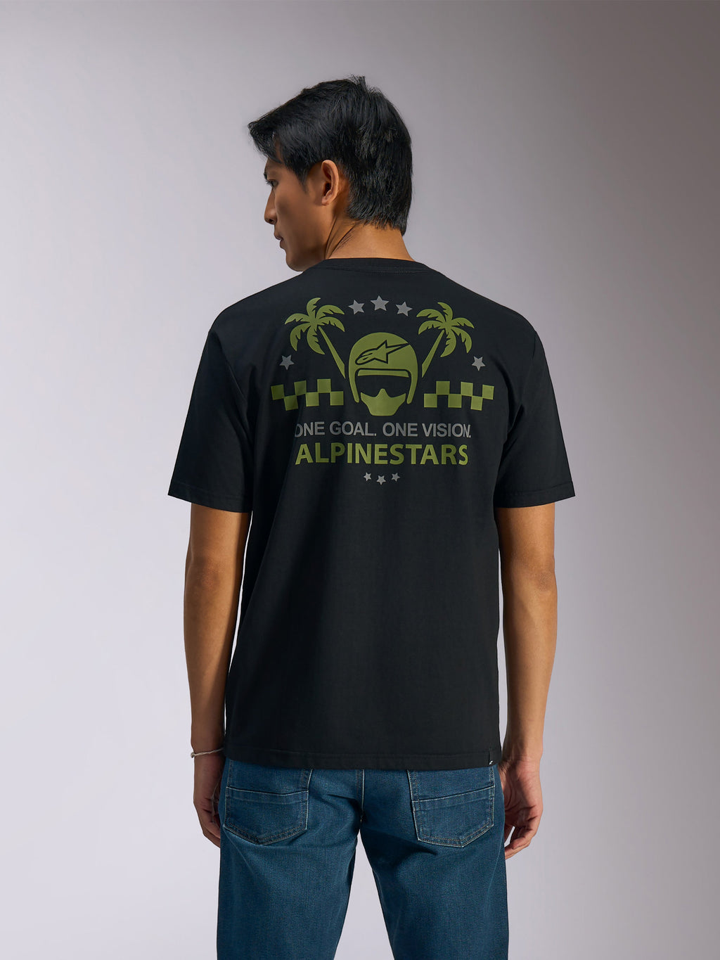 Alpinestars Order CSF Tee, kortärmad t-shirt, svart, vy bakifrån, olivgrön grafik med palmer och hjälmlogotyp, texten "ONE GOAL. ONE VISION. ALPINESTARS", matchad med blå jeans, vardaglig motorsport-streetwear