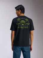 Alpinestars Order CSF Tee, kortärmad t-shirt, svart, vy bakifrån, olivgrön grafik med palmer och hjälmlogotyp, texten "ONE GOAL. ONE VISION. ALPINESTARS", matchad med blå jeans, vardaglig motorsport-streetwear