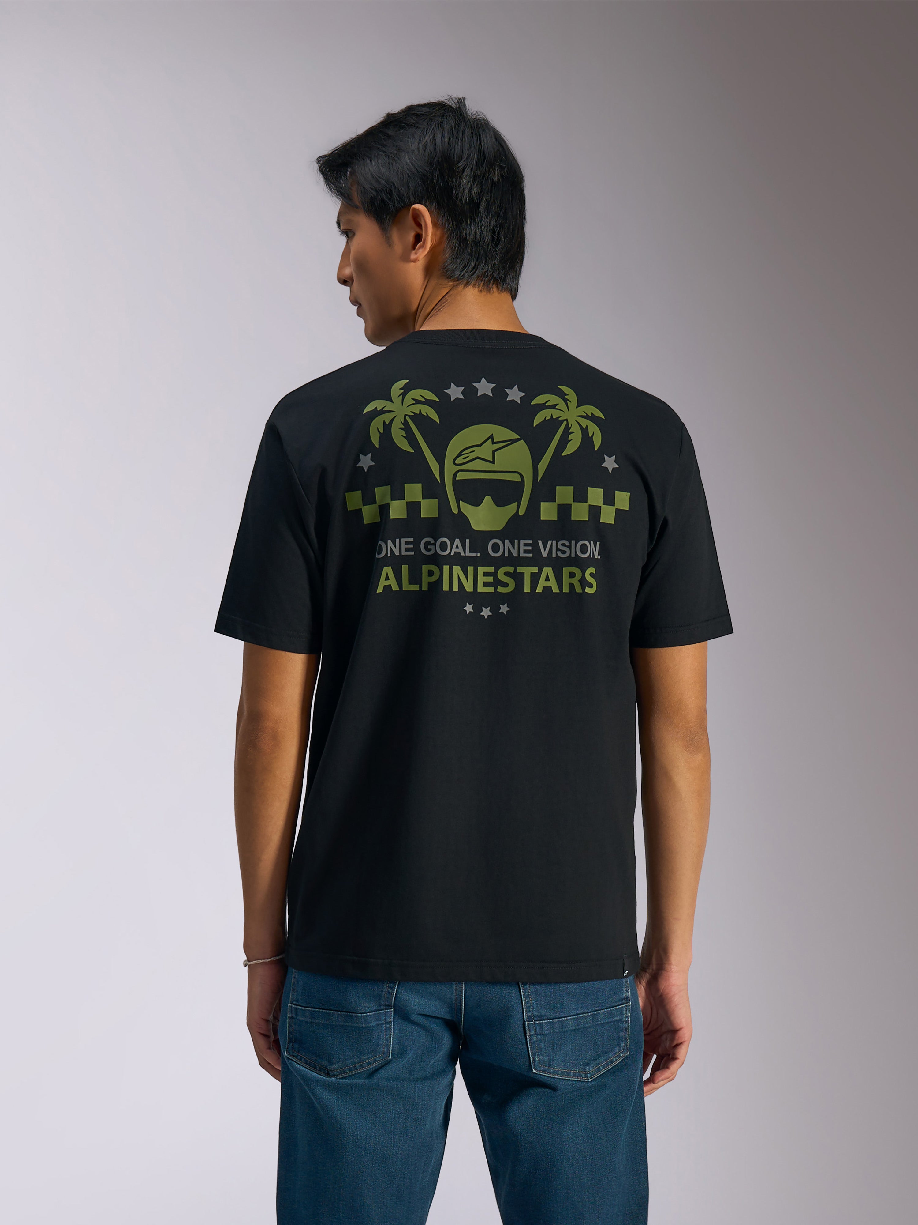 Alpinestars Order CSF Tee, kortärmad t-shirt, svart, vy bakifrån, olivgrön grafik med palmer och hjälmlogotyp, texten "ONE GOAL. ONE VISION. ALPINESTARS", matchad med blå jeans, vardaglig motorsport-streetwear