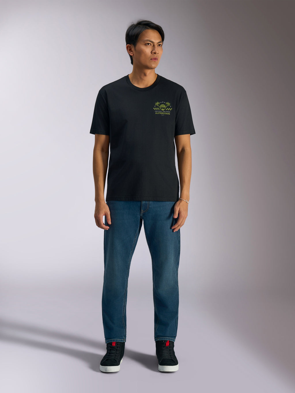 Alpinestars Order CSF Tee, kortärmad t-shirt, svart, limegrön grafik med hjälm och palmträd på bröstet, bärs med blå jeans och svarta sneakers, casual motorsport streetwear