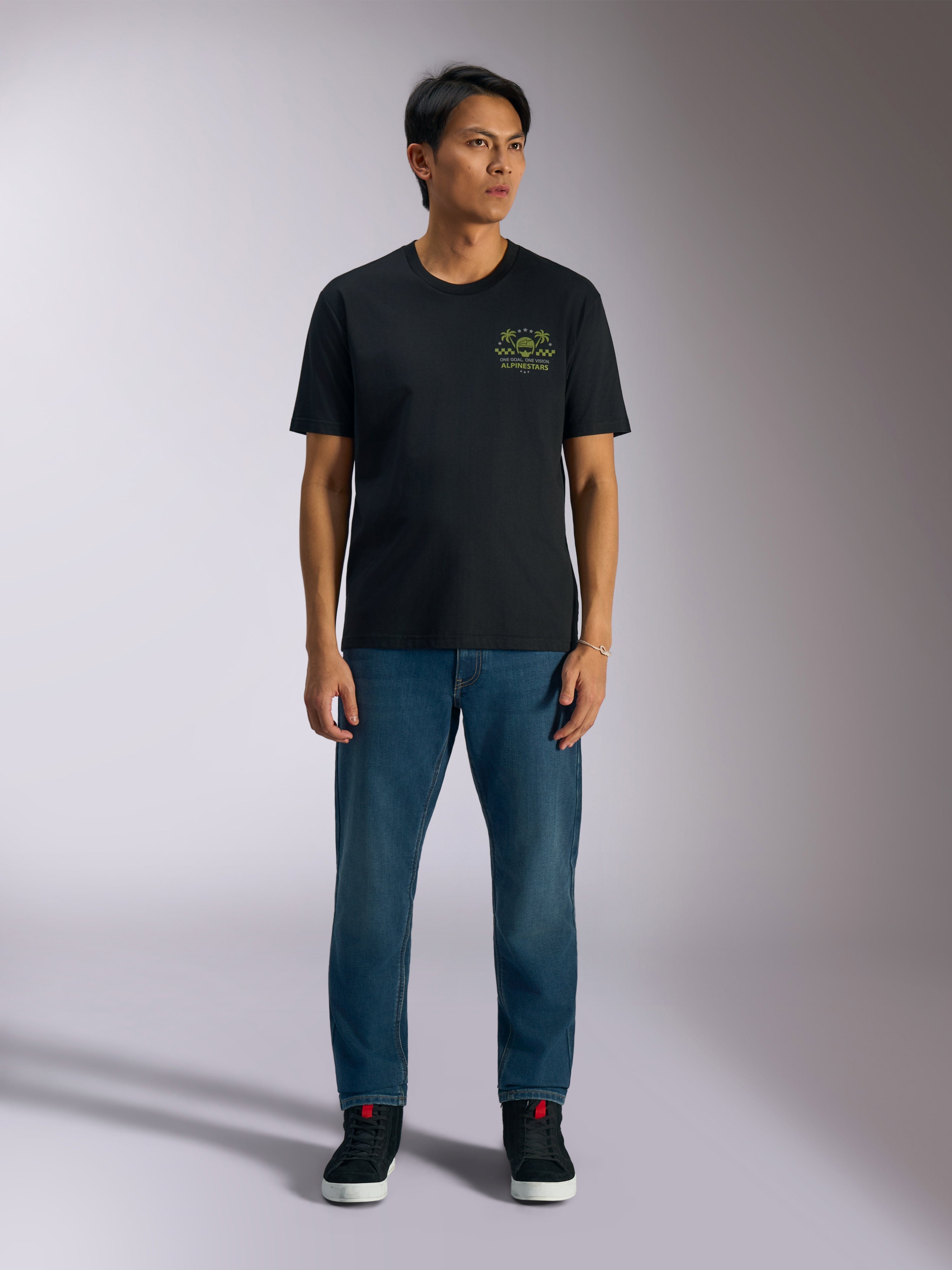 Alpinestars Order CSF Tee, kortärmad t-shirt, svart, limegrön grafik med hjälm och palmträd på bröstet, bärs med blå jeans och svarta sneakers, casual motorsport streetwear