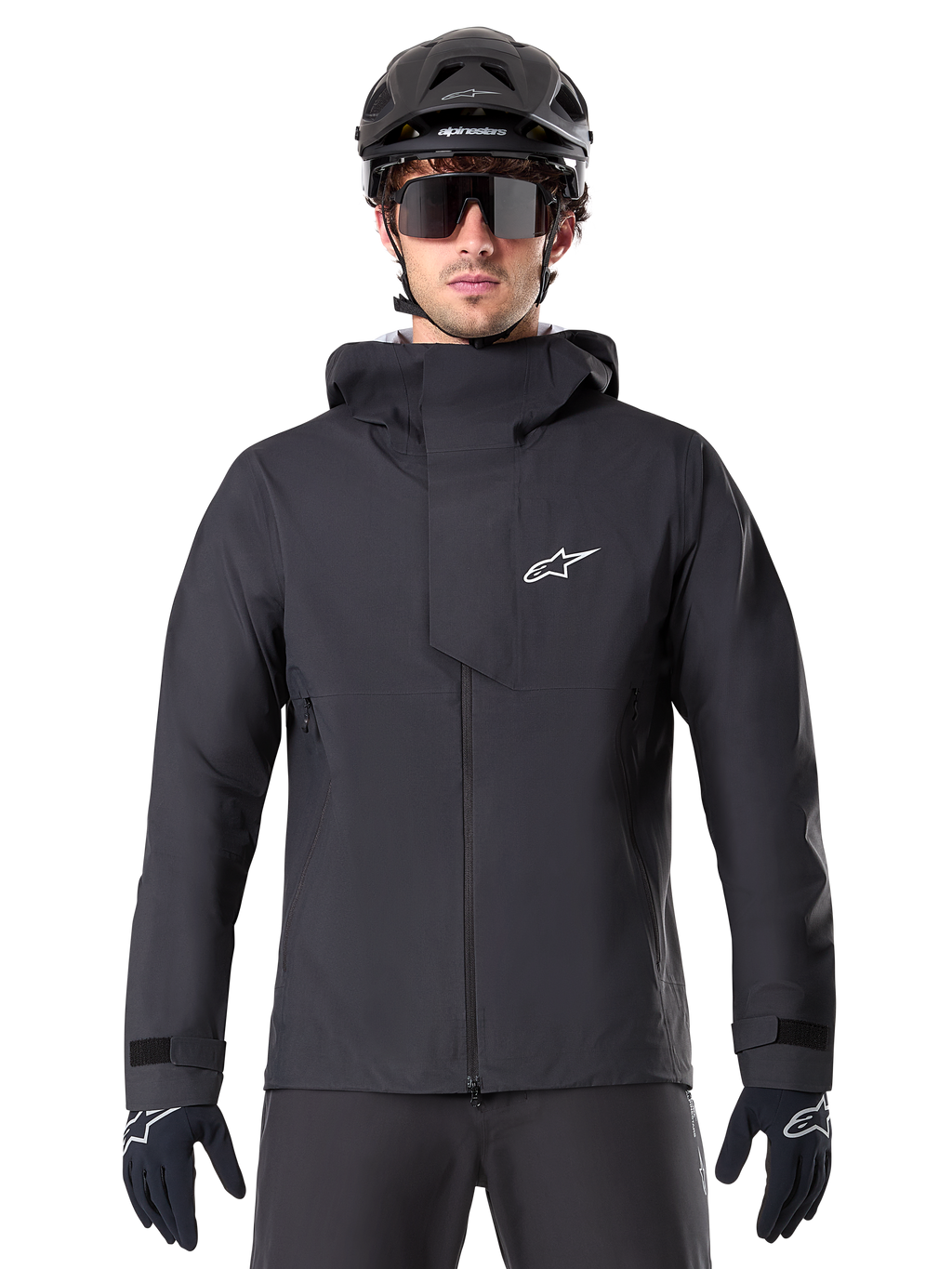 Alpinestars A-Dura Elite vattentät jacka, svart MTB-jacka, design med hög krage och huva, dragkedja fram med skyddande bröstflik och vit logotyp, bärs med svart hjälm och cykelhandskar, tekniskt väderskydd för trailcykling